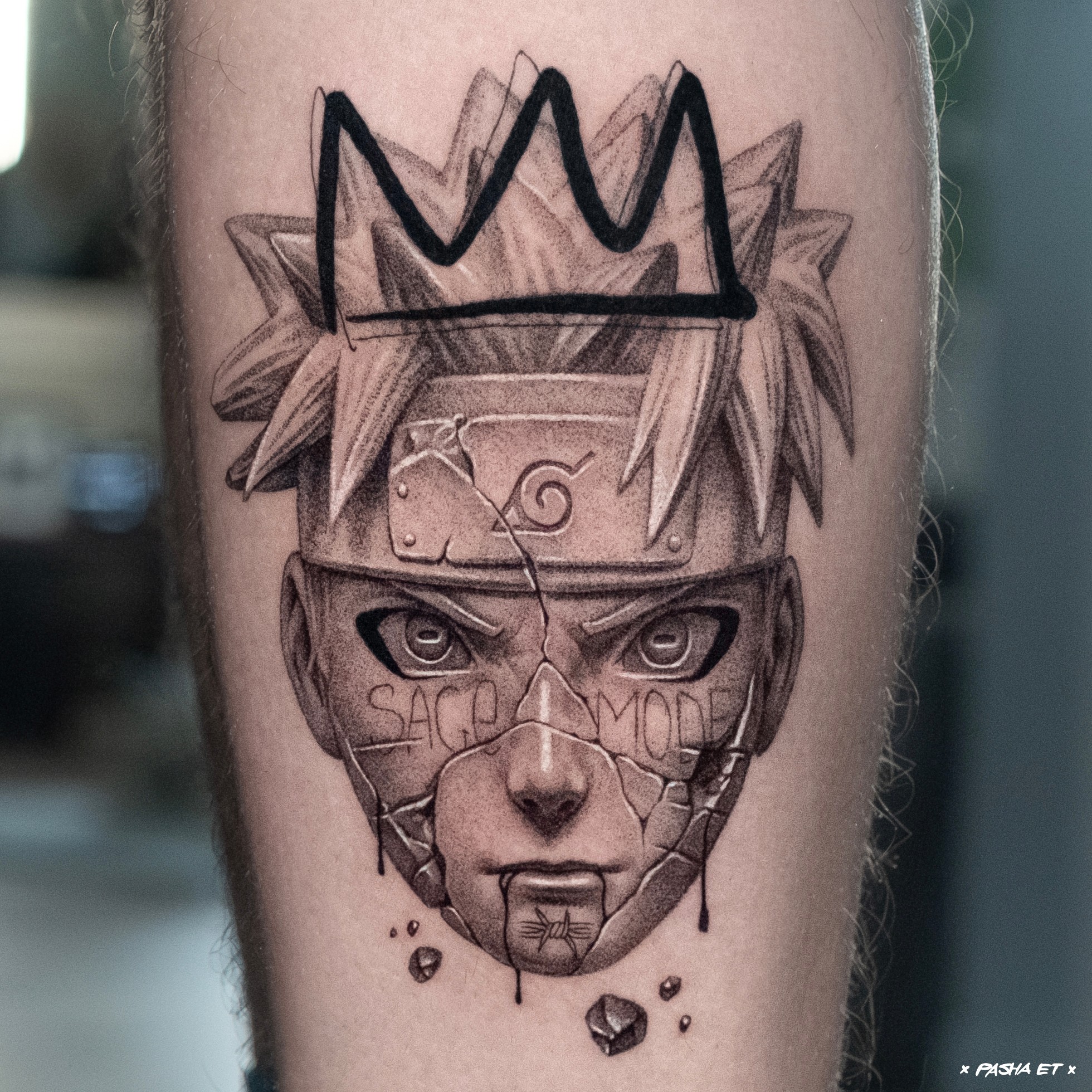 Tattoo of a stylized face with a crown above, featuring detailed eyes, nose, mouth, and cracks, with text on the forehead.