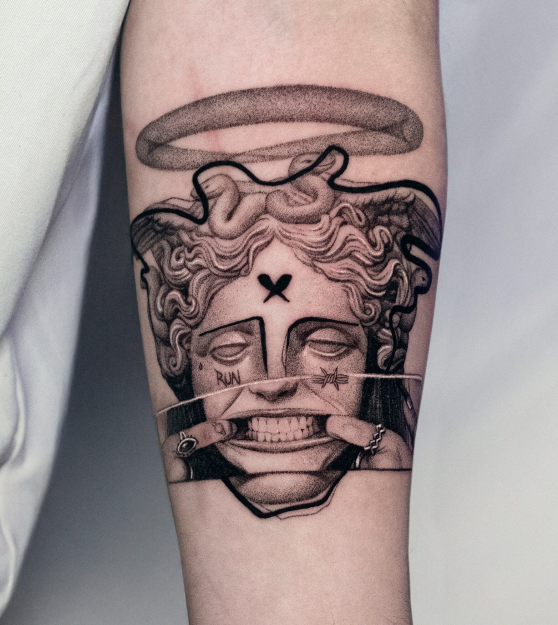 Tattoo of a face with a halo, angel wings, and a finger covering the mouth, with detailed line work and shading.