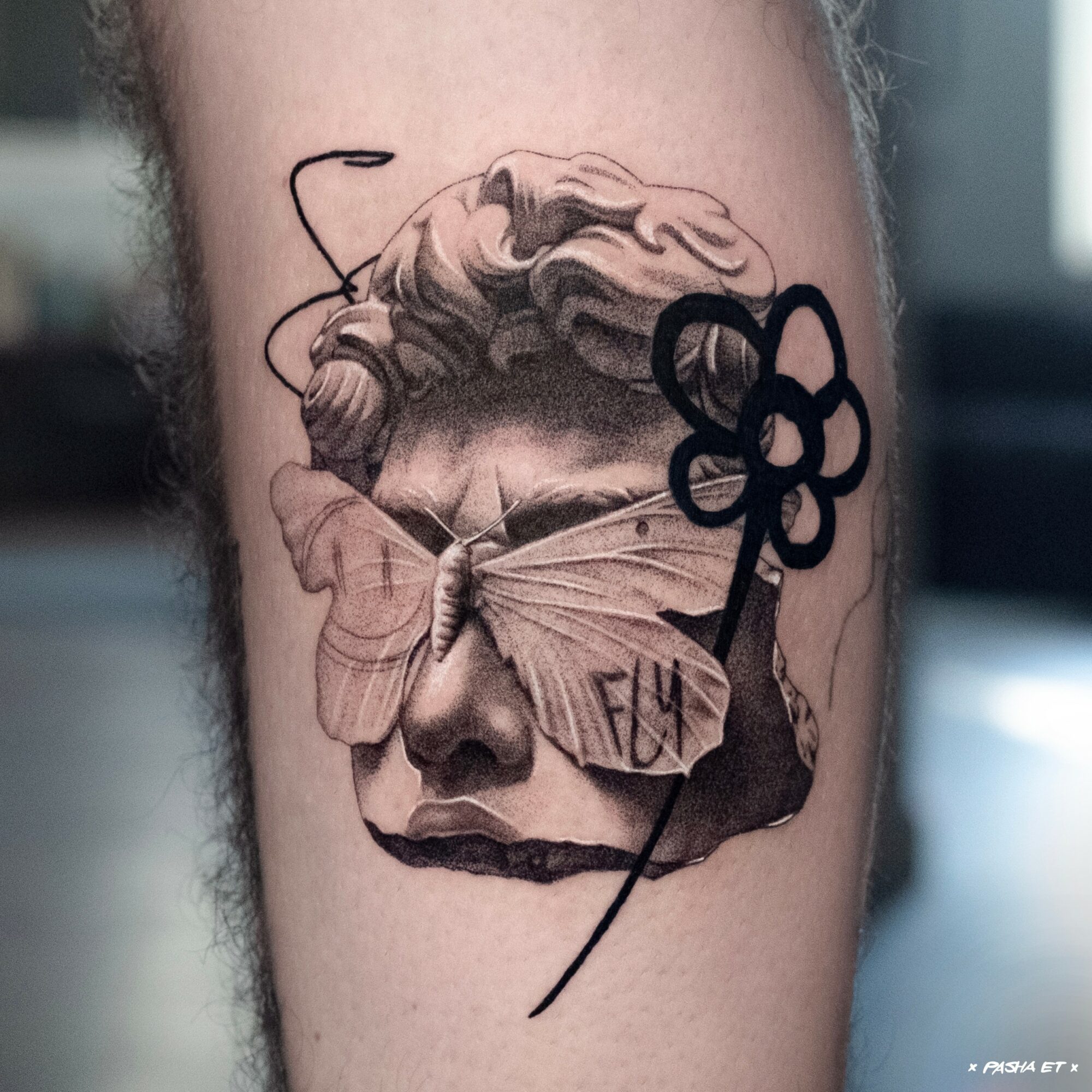 Tattoo of a butterfly with a woman's face and a key, in black and gray, on skin.