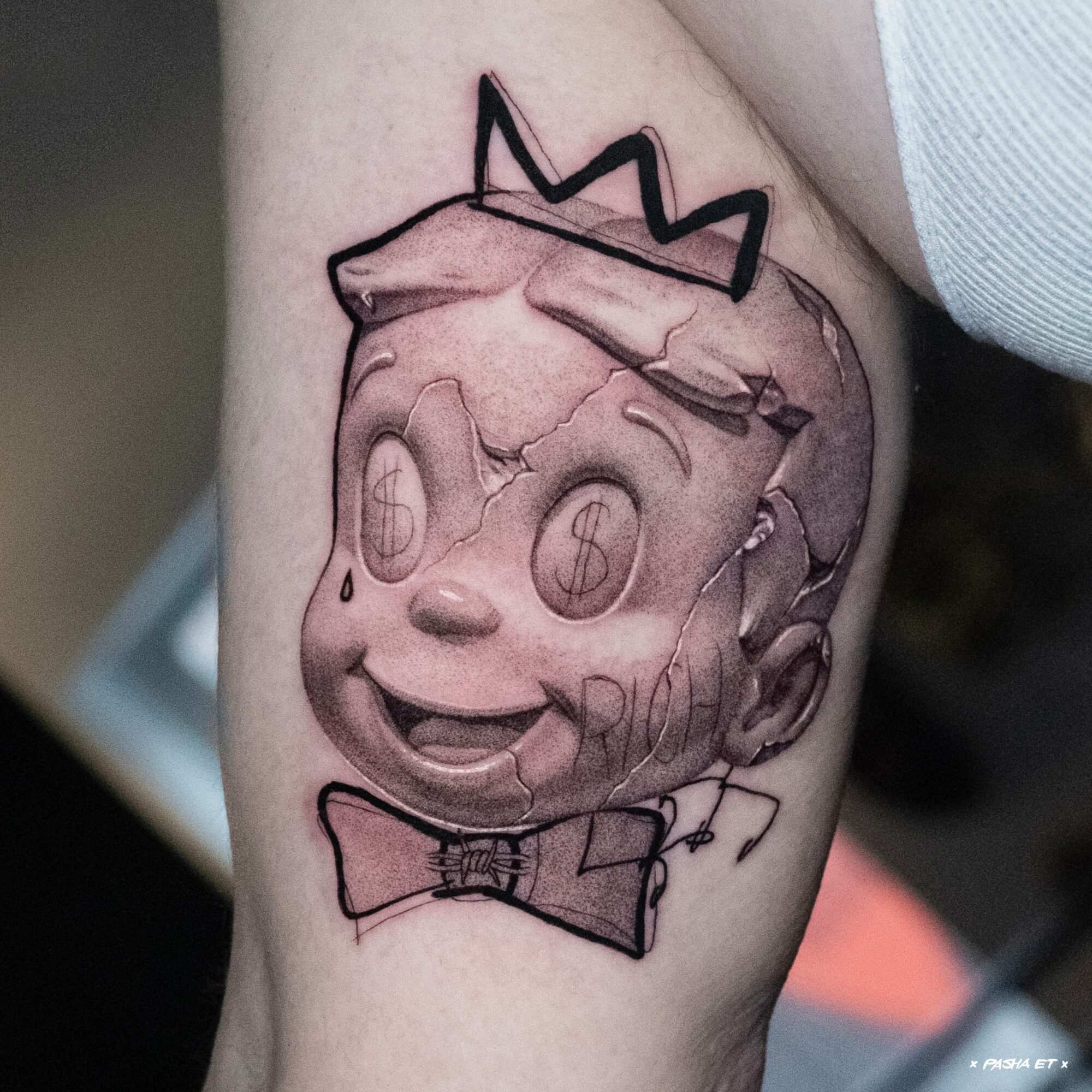Cartoon-style character with a crown, smiling face, and bow tie, drawn in black ink on skin.