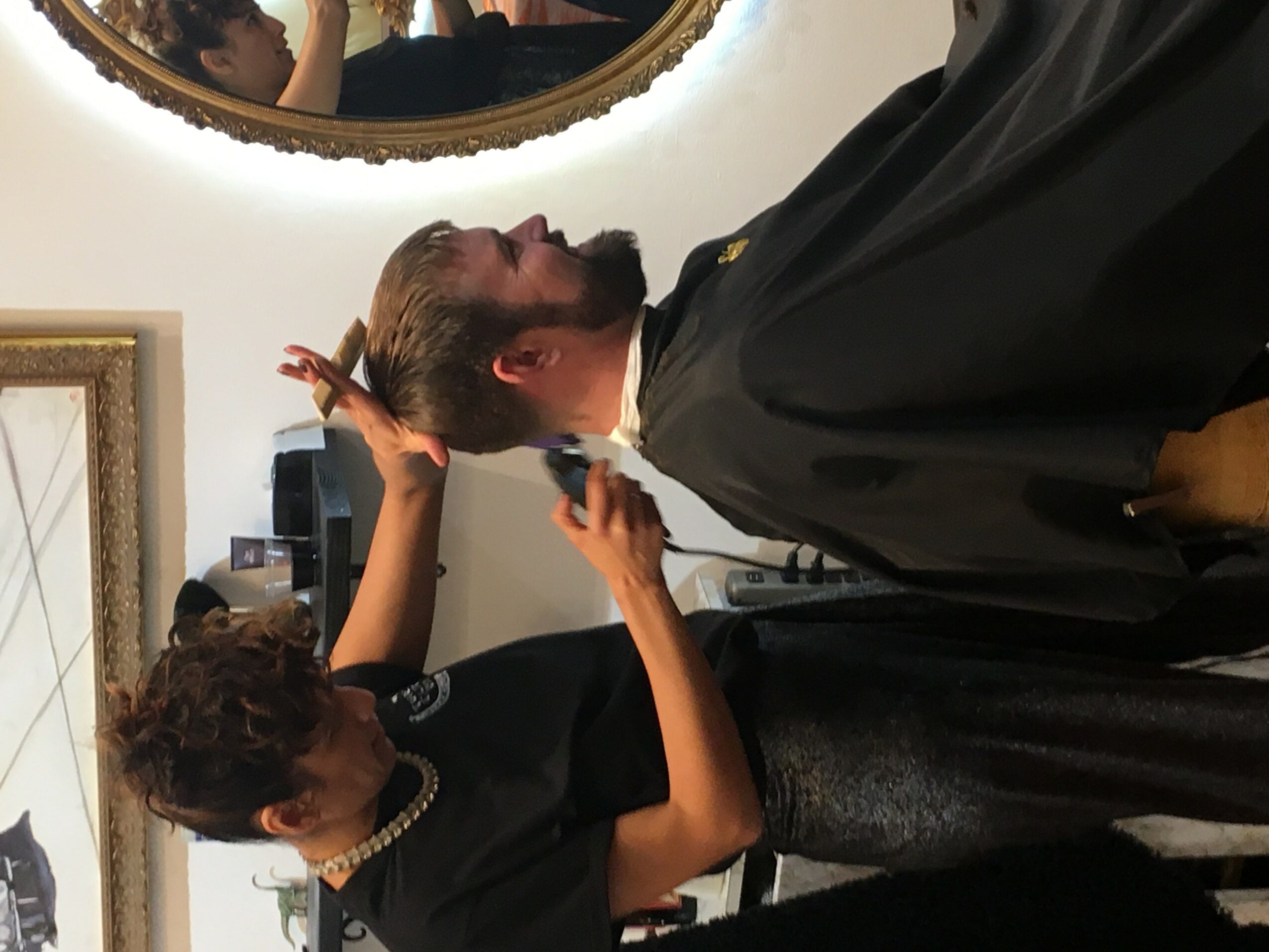 Person getting a haircut in a salon, with a mirror reflecting their face and hair, and a stylist working on their hair.