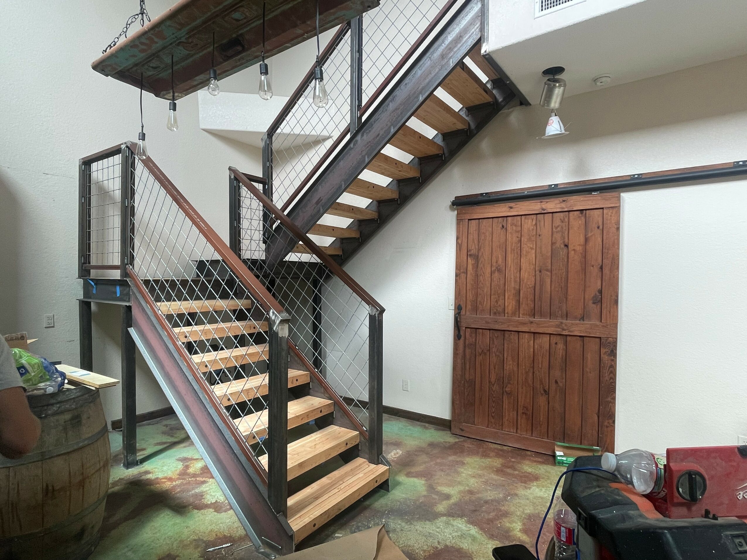 Indoor staircase with wooden steps, metal railing, and a wooden cabinet beneath the stairs, with a light fixture above.