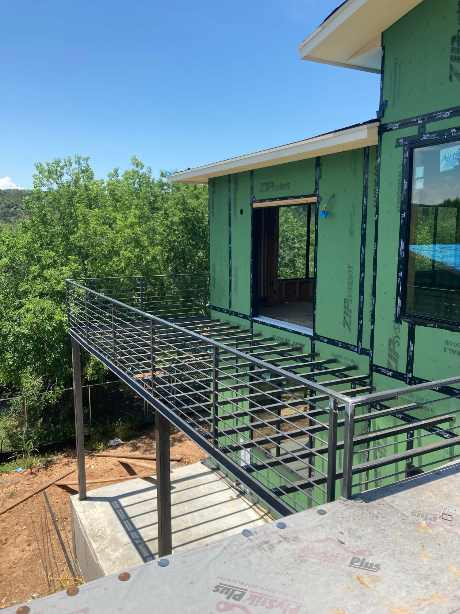 Construction site with green framing and metal railing, outdoor setting with trees in background.