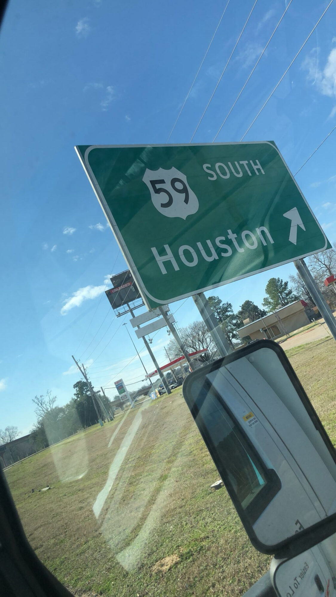 Green highway sign indicating southbound US Route 59 toward Houston, with a clear blue sky and trees in the background.