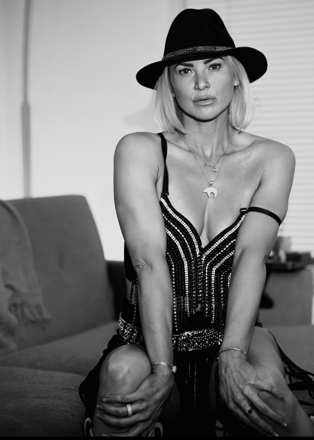 Woman wearing a hat and dress, sitting on a couch, looking at the camera, in black and white.