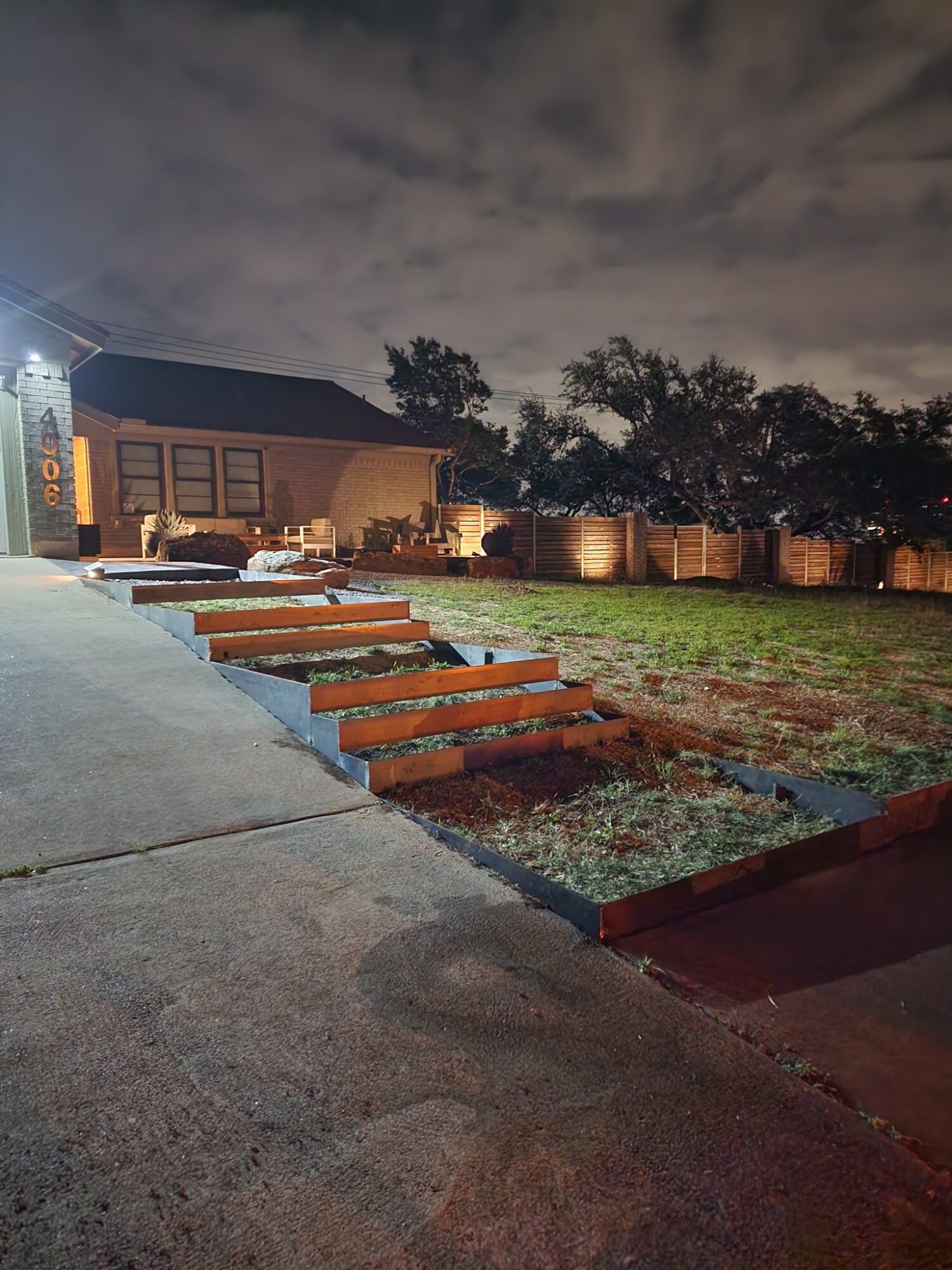 Nighttime view of a backyard with steps leading to a house, trees, and a cloudy sky.