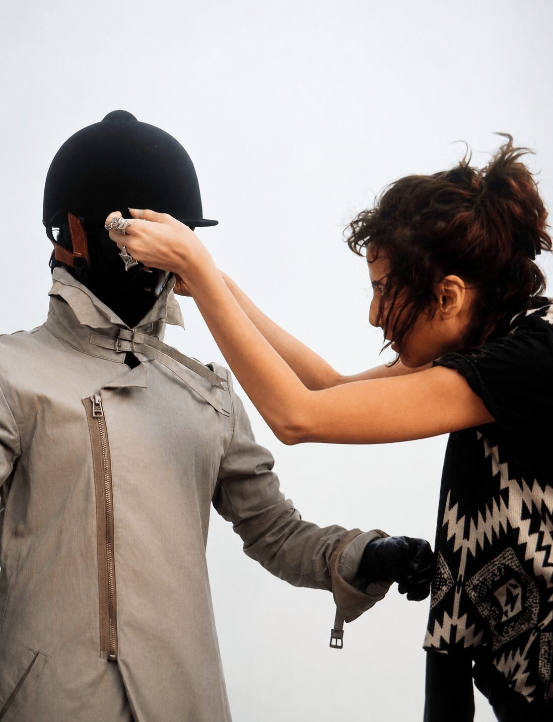 Woman adjusting a person wearing a helmet and mask, with a plain light background.