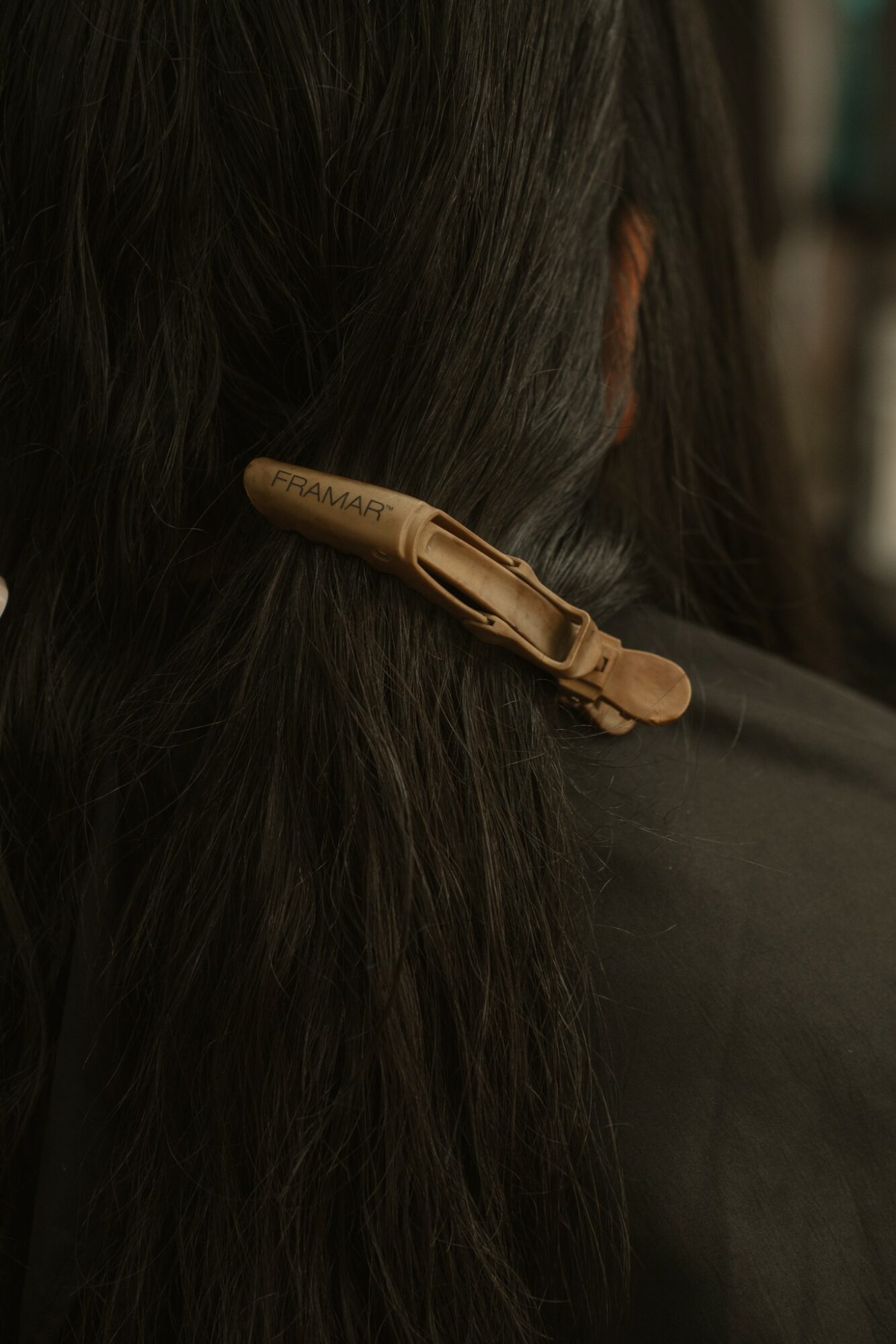 Close-up of a person's dark hair with a beige hair clip holding hair back, background blurred