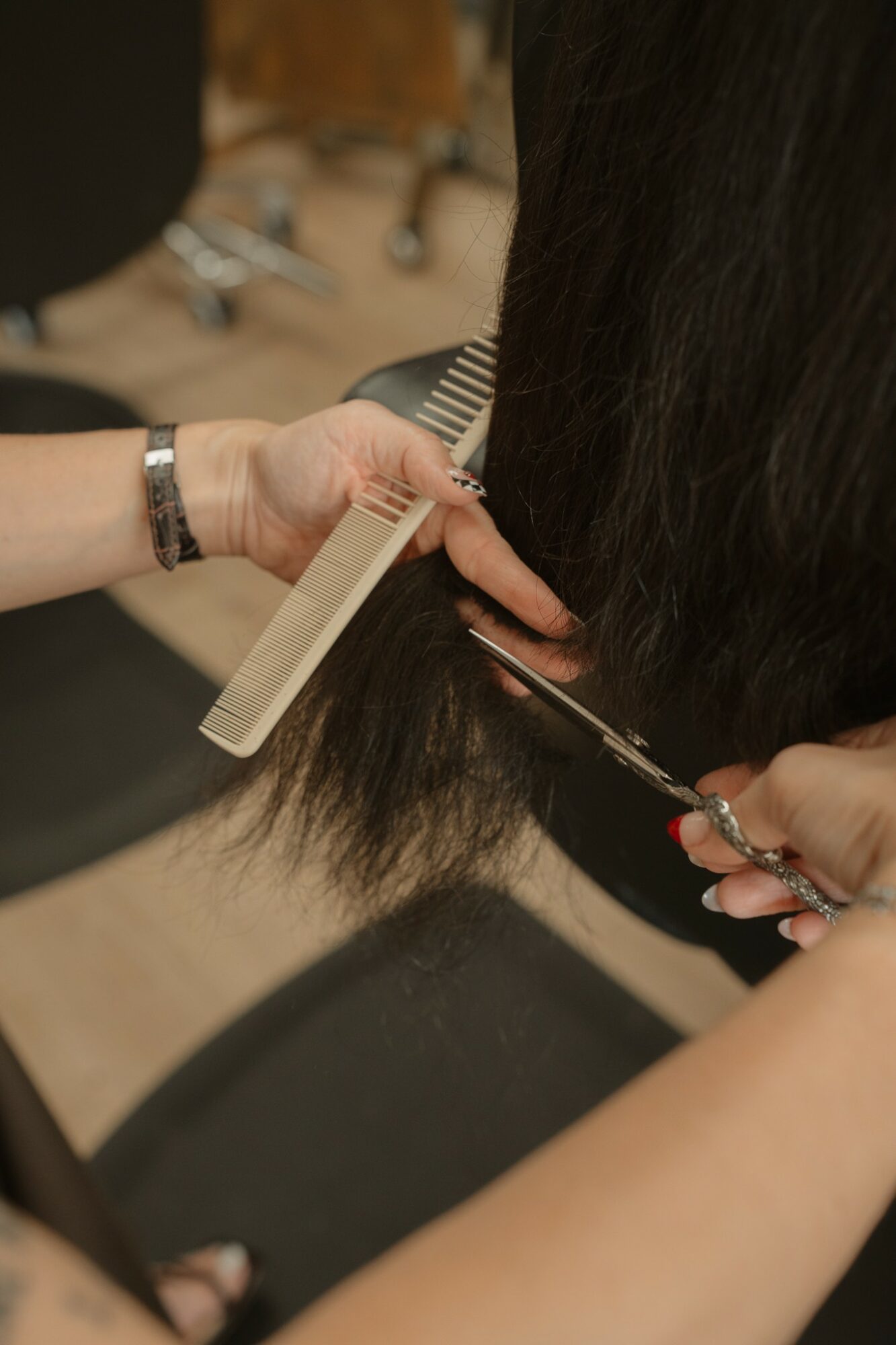 Person cutting hair with scissors and comb, focusing on hair and hands, in a salon setting.