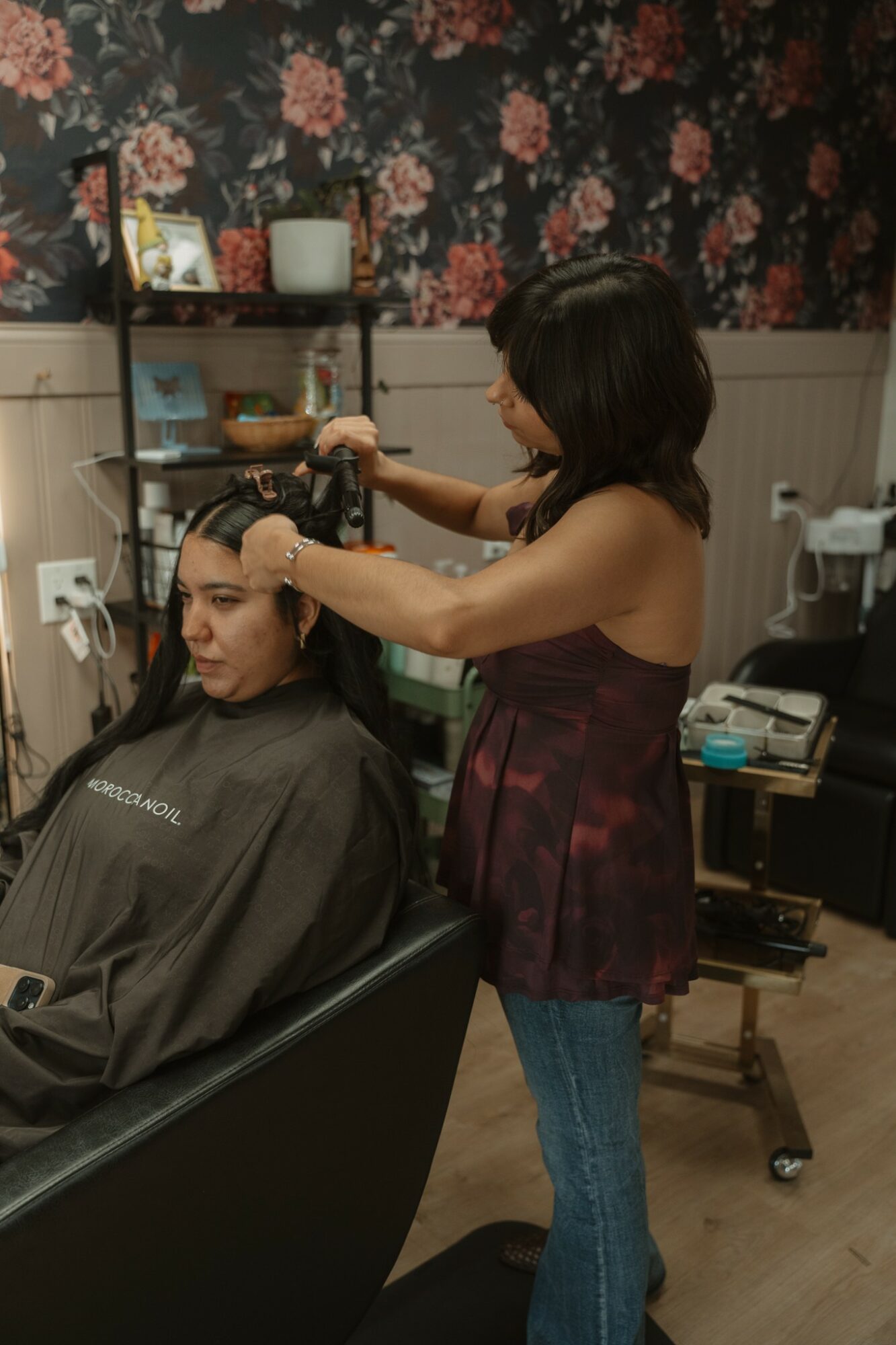 A woman receives a haircut in a salon, sitting in a chair with a cape, while a stylist works on her hair.