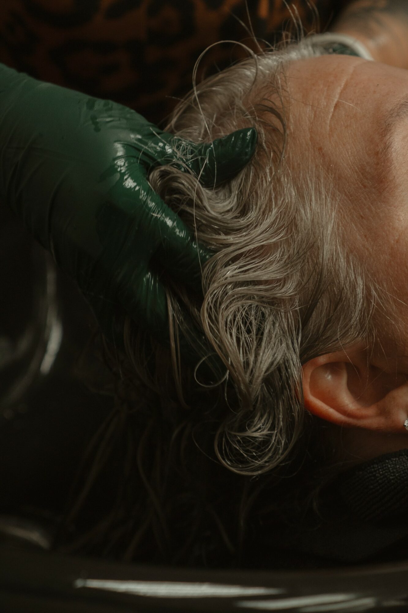 Person receiving a scalp treatment with a gloved hand holding hair, close-up of head and hair.