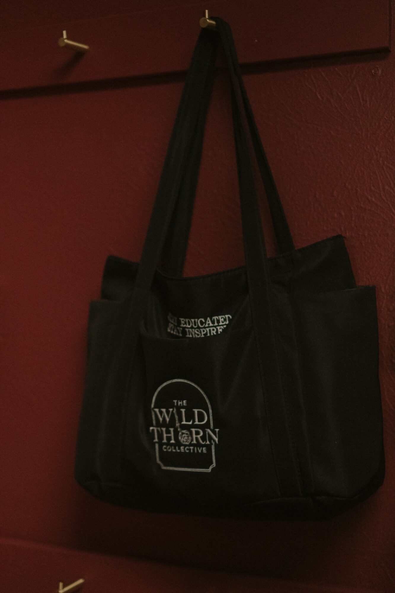 Black tote bag hanging on a wall with text and logo, against a red background.