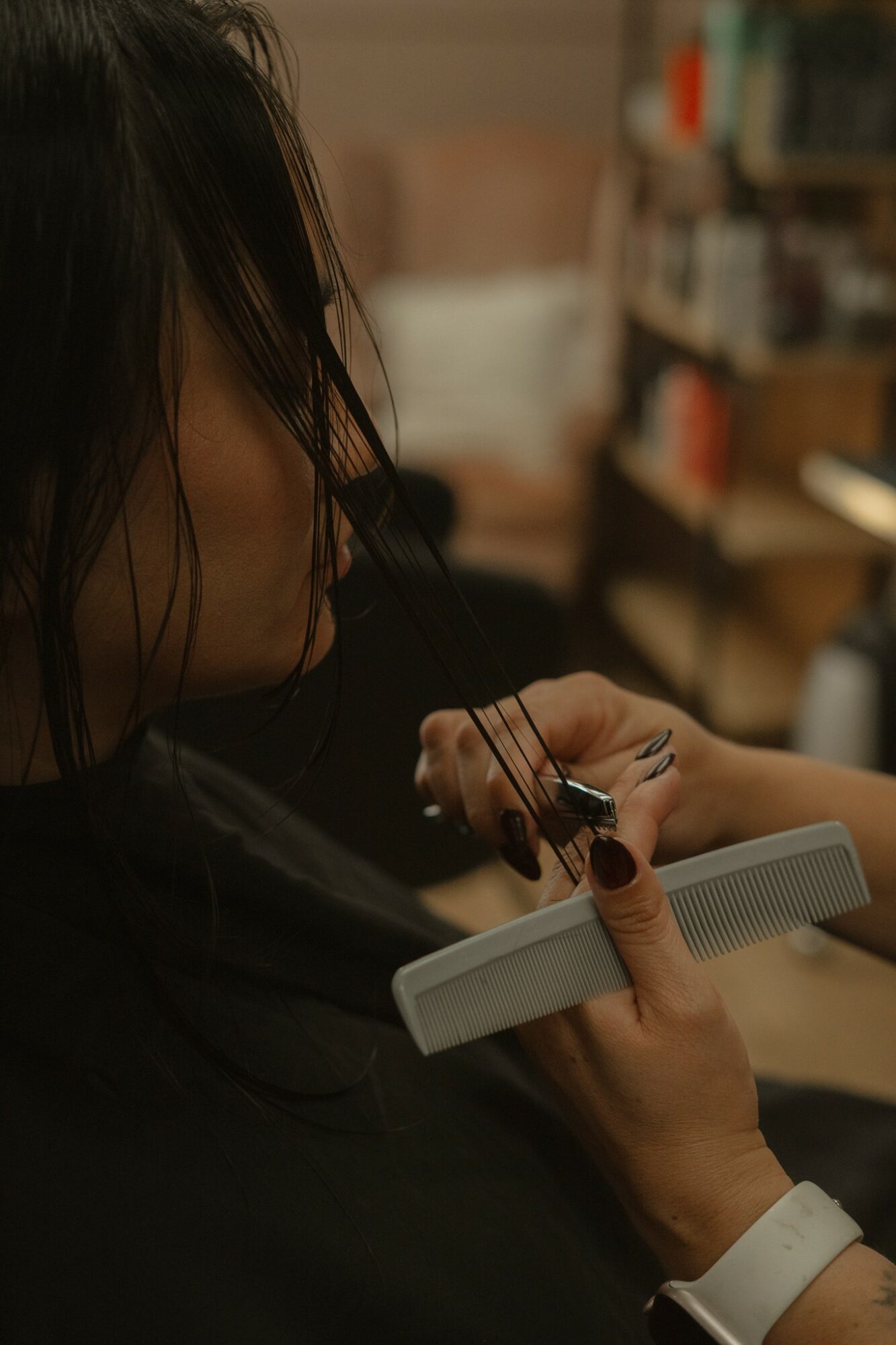 Person with dark hair holding a hairbrush and a mirror, in a room with shelves and books.