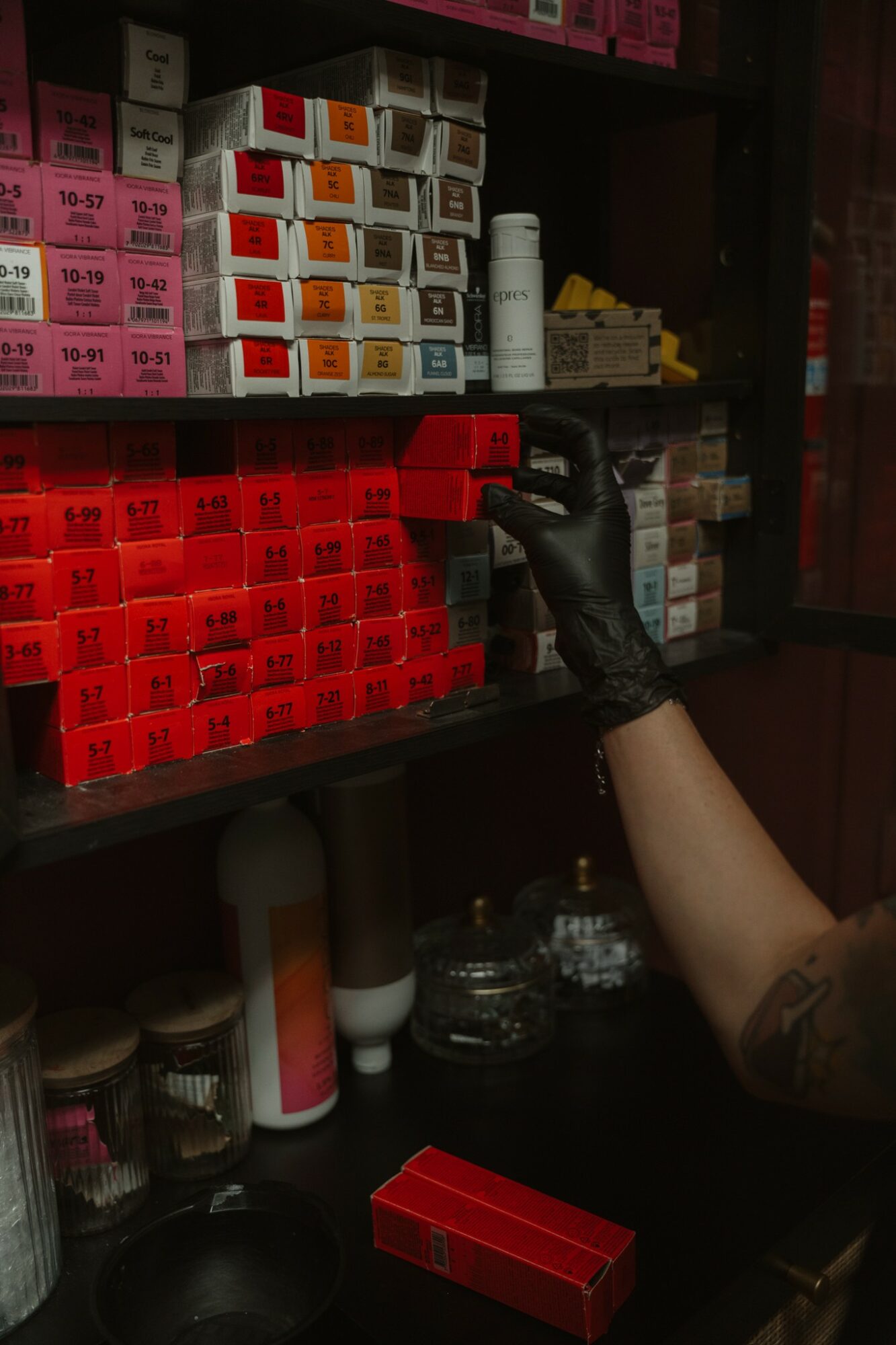 Person wearing a black glove reaching for small boxes on a shelf in a pharmacy or store.