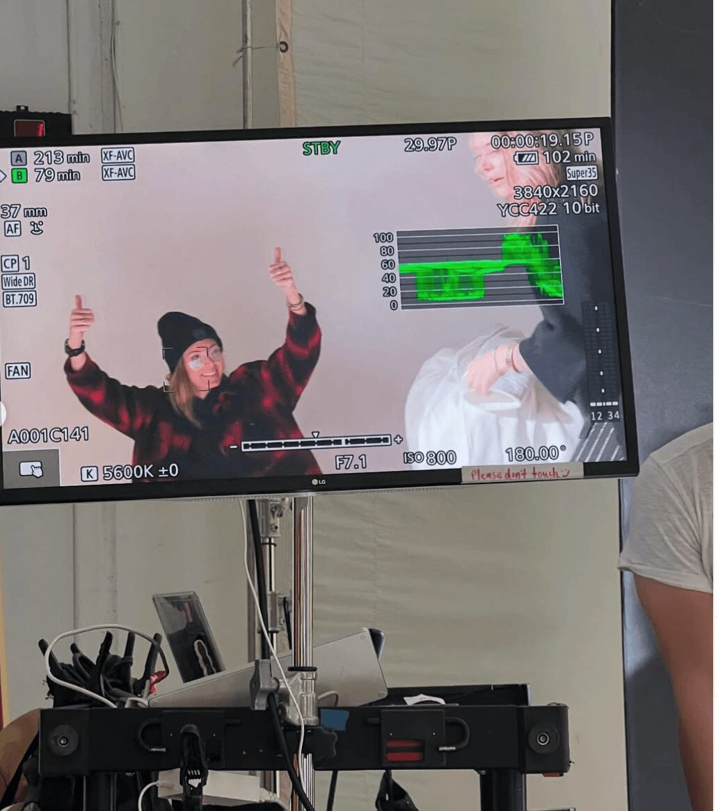 Two people on a screen, one wearing a beanie and jacket, gesturing with hands, in a studio setting.