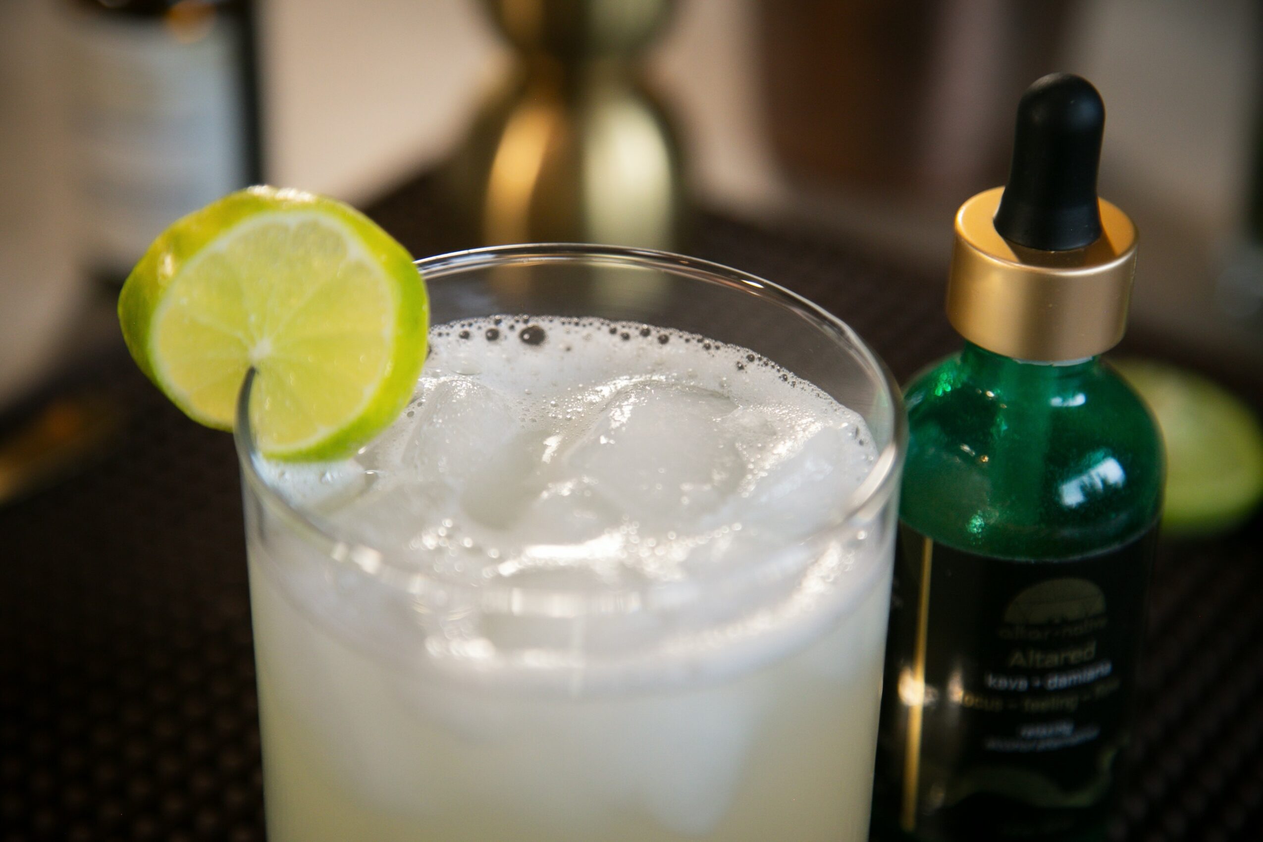 A glass with a lime wedge on the rim, filled with a cloudy beverage and ice, on a dark surface.