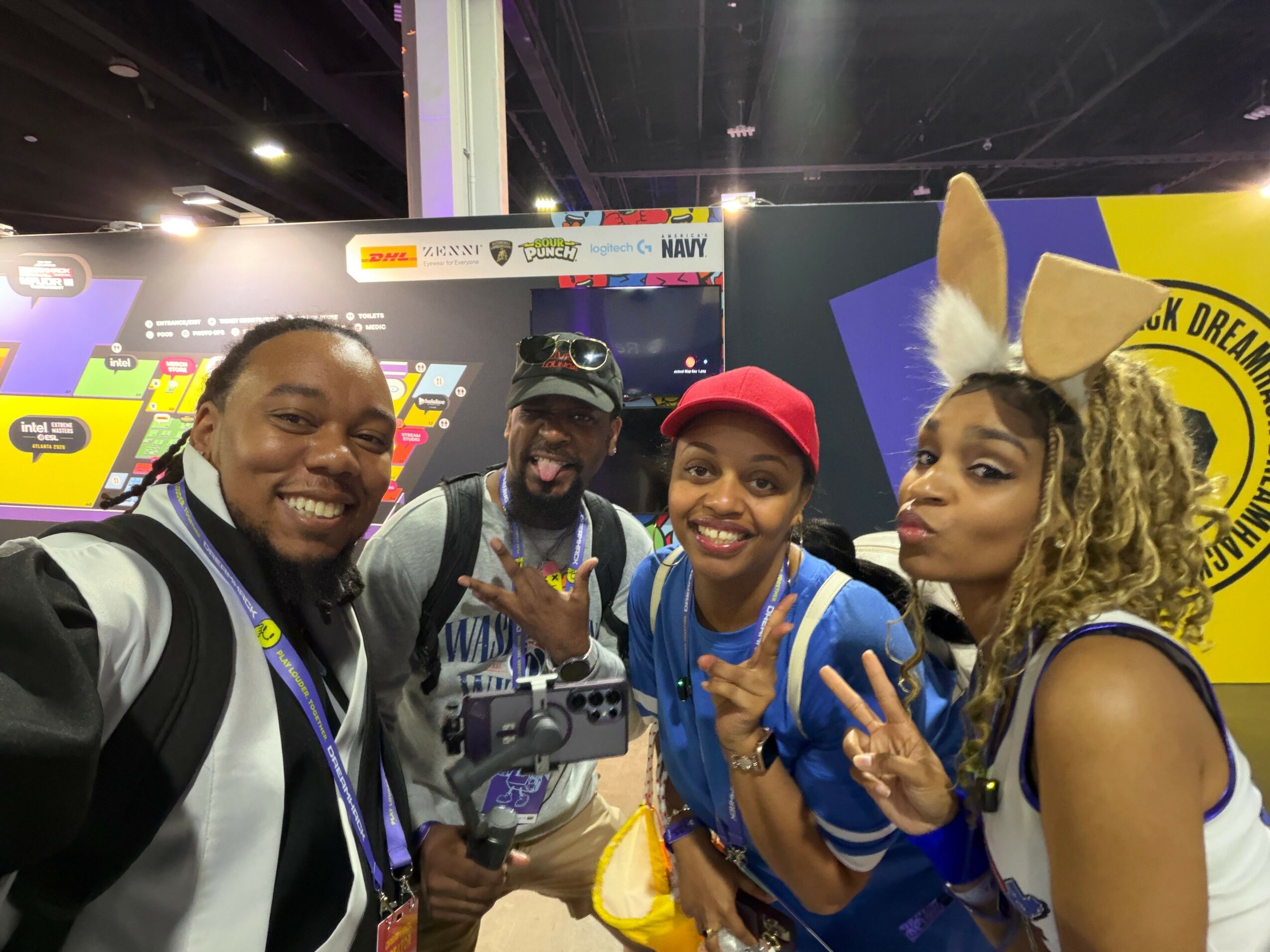 Four people posing at an event, with colorful banners and displays in the background.