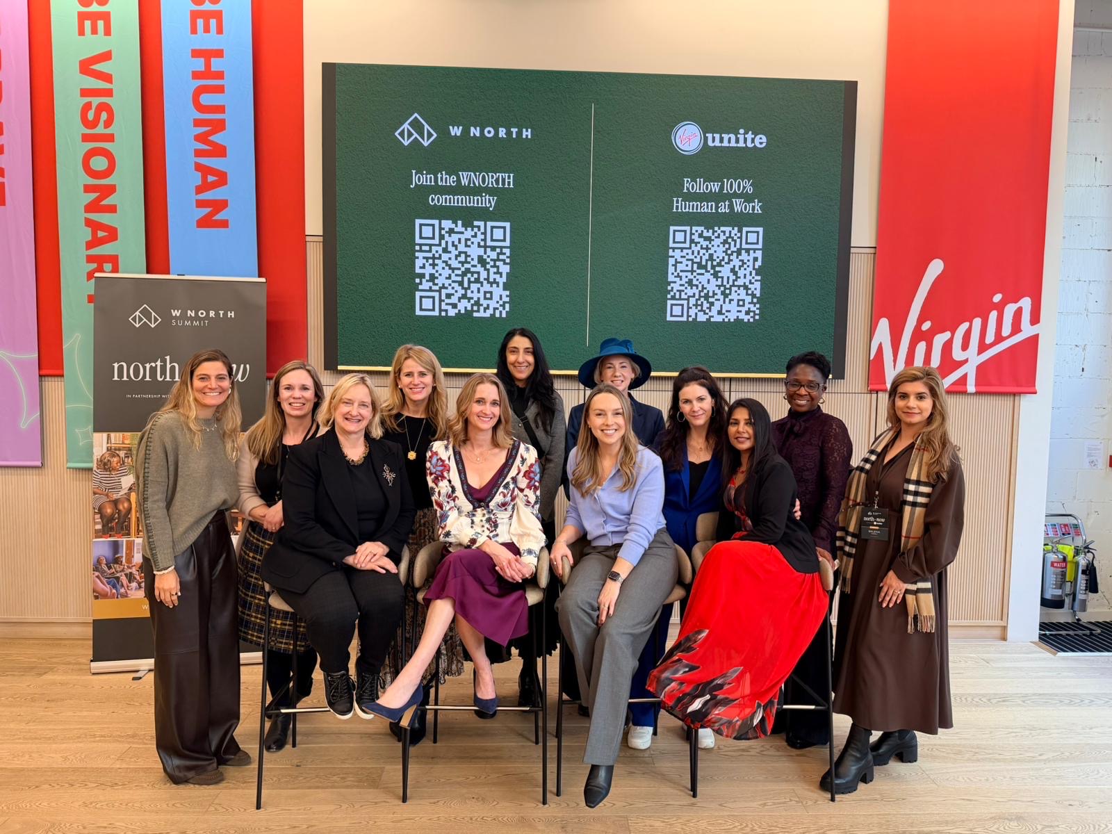 Group of ten women posing indoors with a digital screen behind them displaying QR codes and logos.