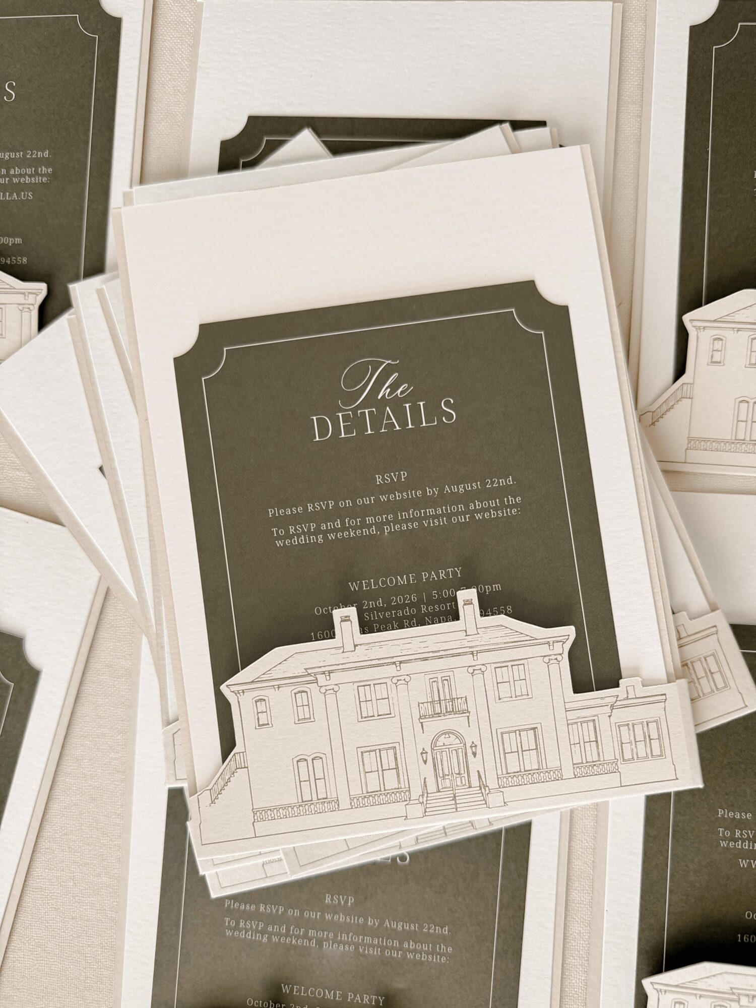 Stack of wedding details cards with a building illustration, gray background, and elegant font, arranged on a table.