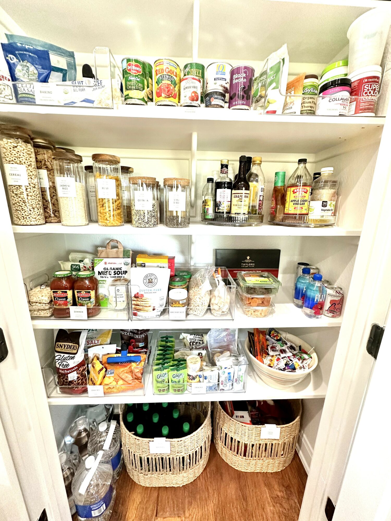 Pantry shelf filled with jars, bottles, and containers of food and condiments, organized on three shelves.