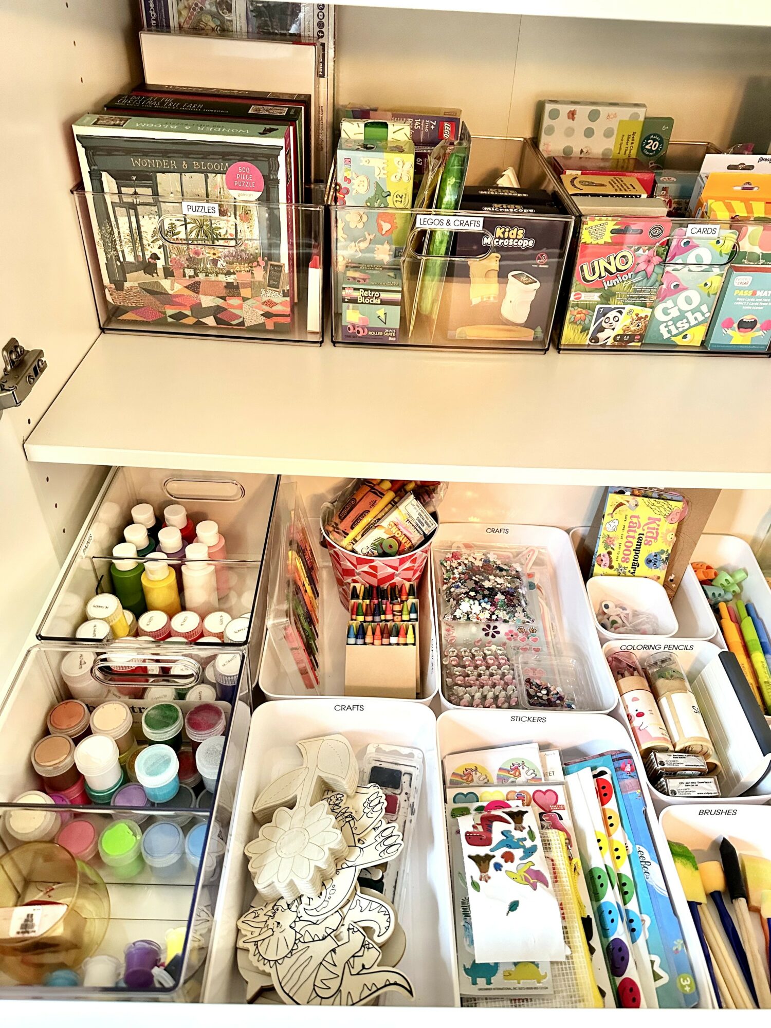 Shelves with art supplies, including paints, markers, coloring pages, and craft materials, organized in containers and on the surface.