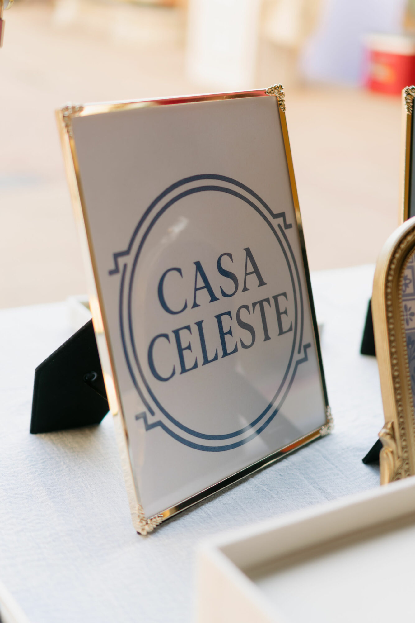 Framed sign with the text 'Casa Celeste' on a table, with blurred background and a partial view of a chair.