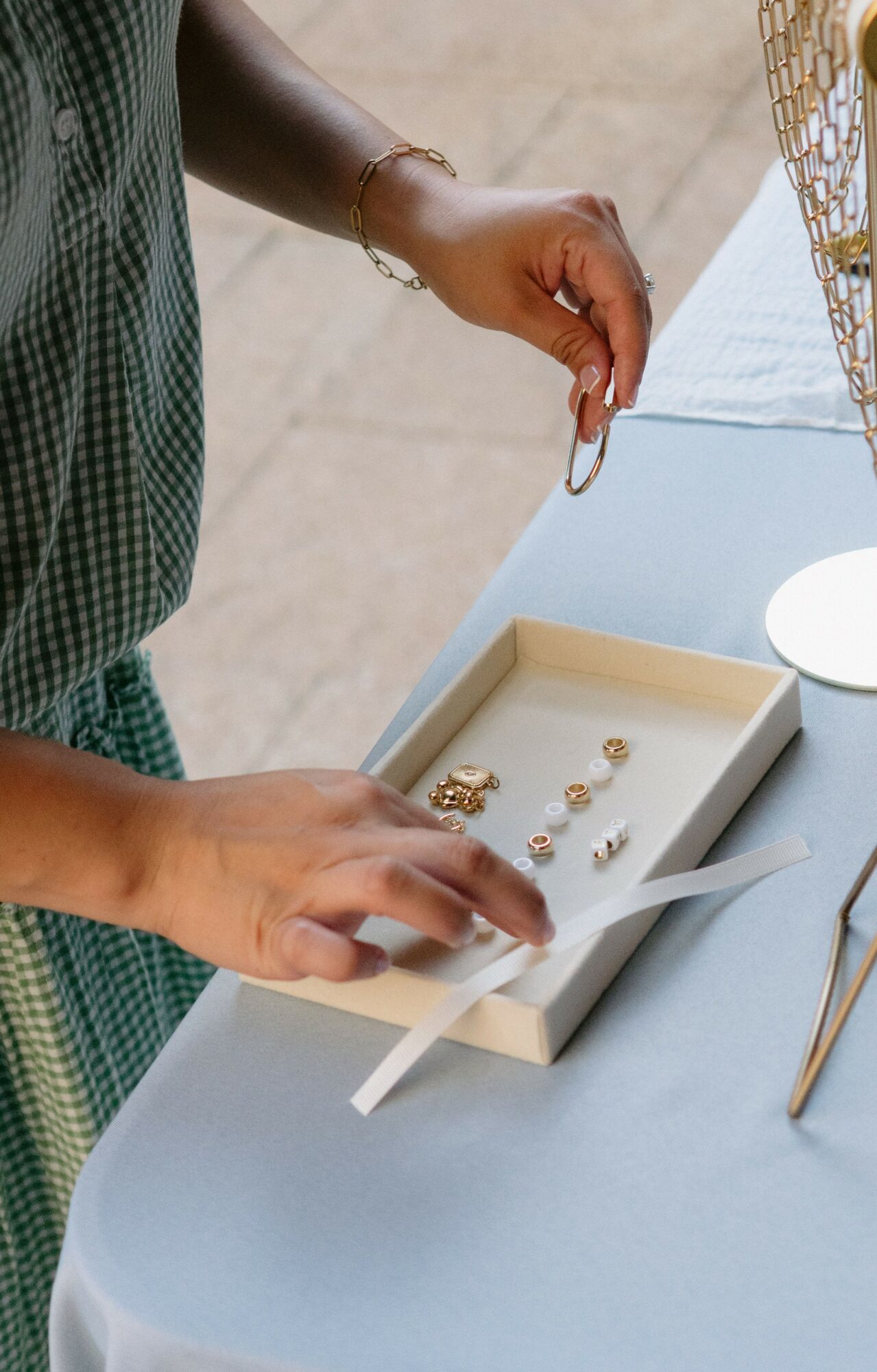 Person's hands selecting jewelry from a tray on a table, with a white box and other items nearby.