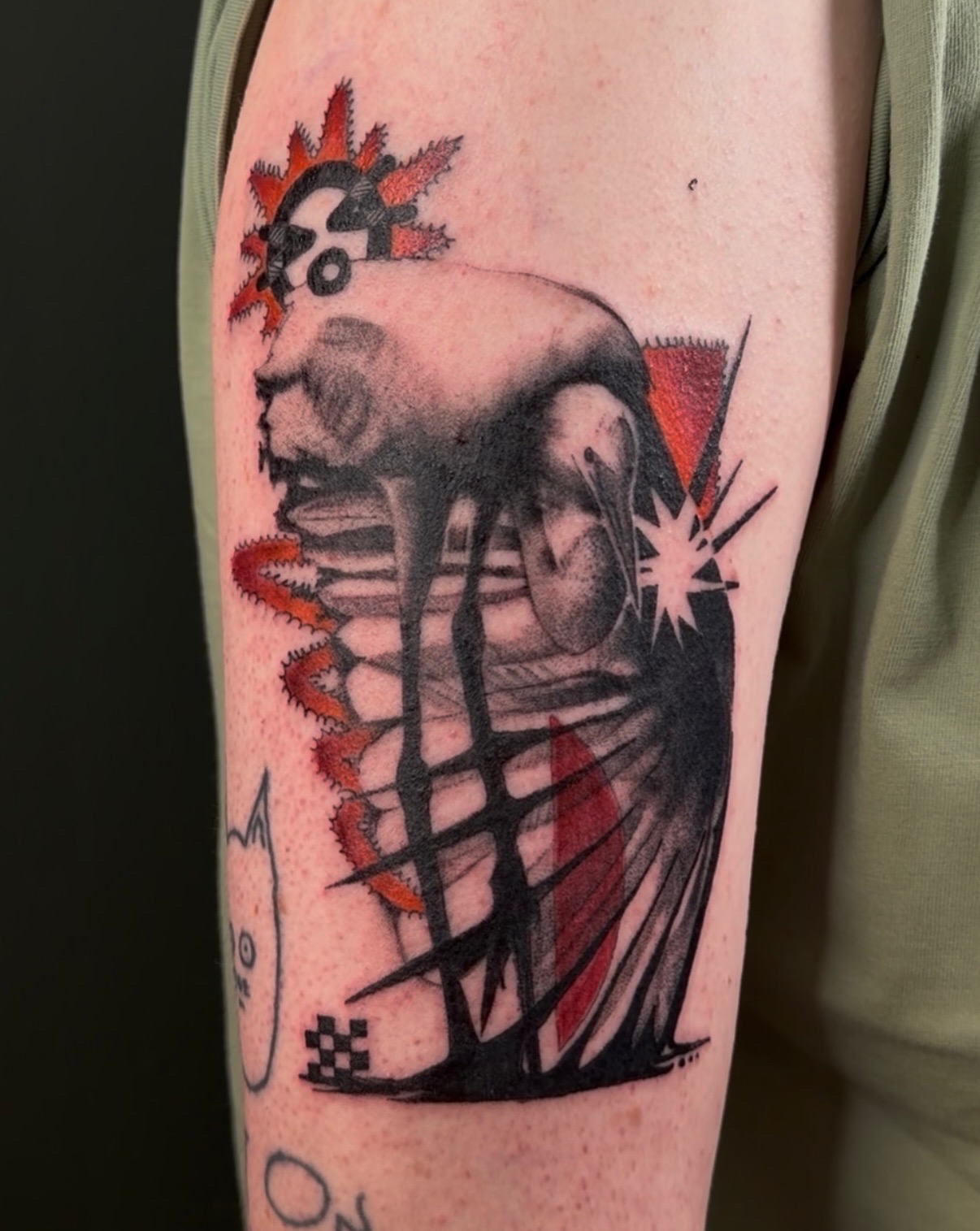 Tattoo of a skull with a colorful explosion, abstract shapes, and a starburst, in black, red, and orange colors.
