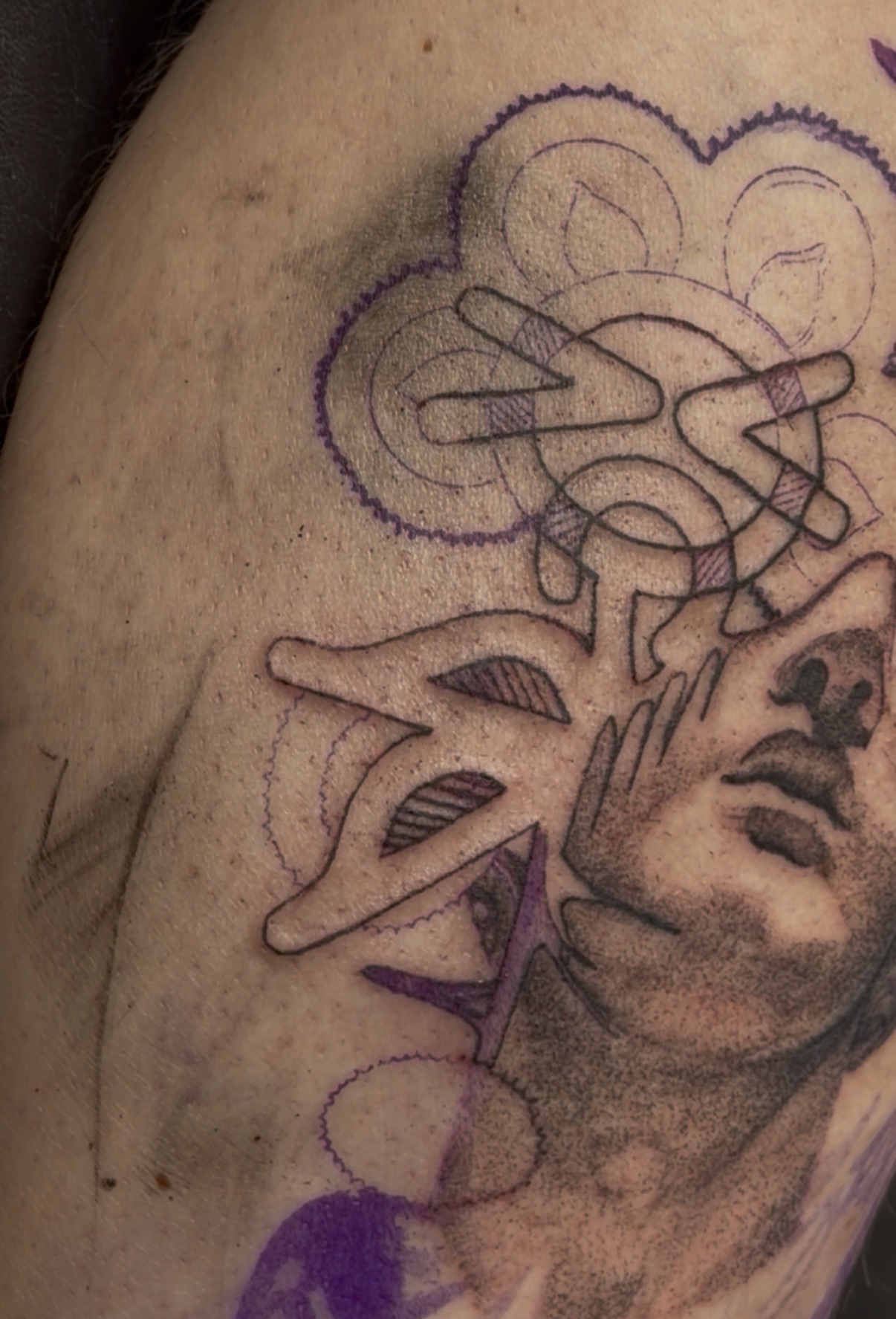 Tattoo sketch of a face with abstract shapes and a cloud outline above, on skin with some shading and lines.