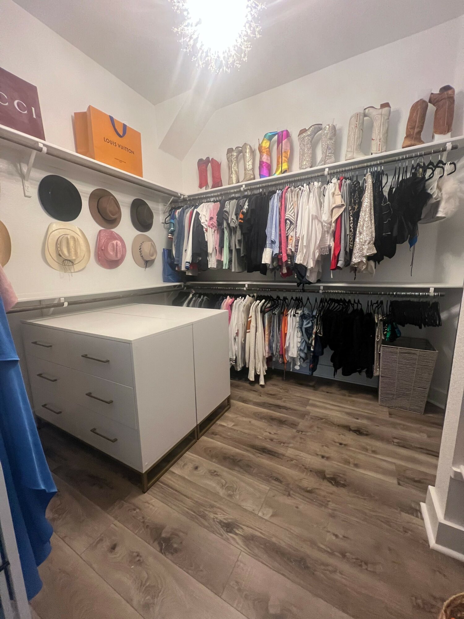 Clothing store with shelves of folded clothes and hanging garments, white drawers, and wooden flooring.