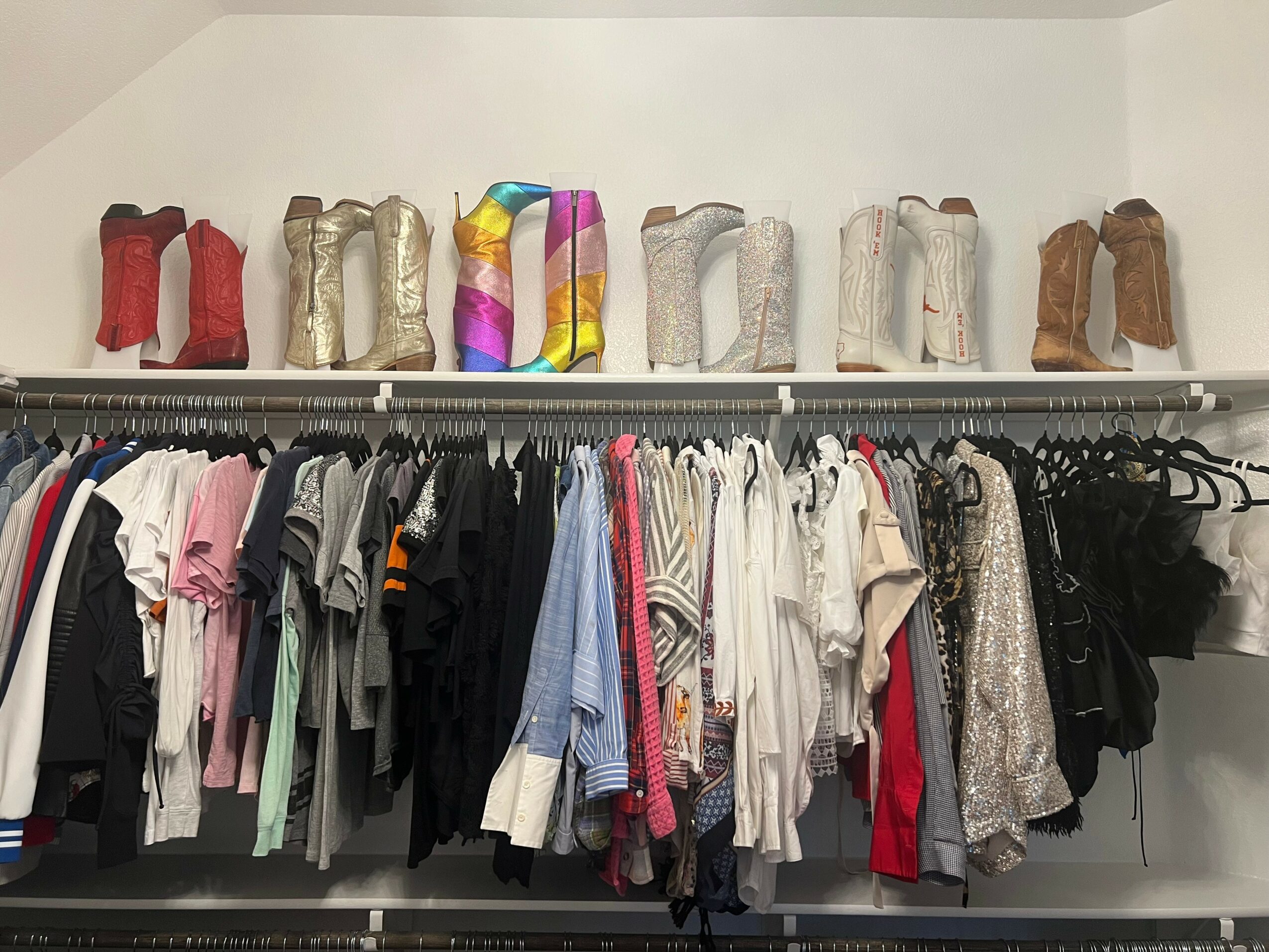 Clothing rack with various shirts and jackets, and a shelf with colorful and neutral boots above.