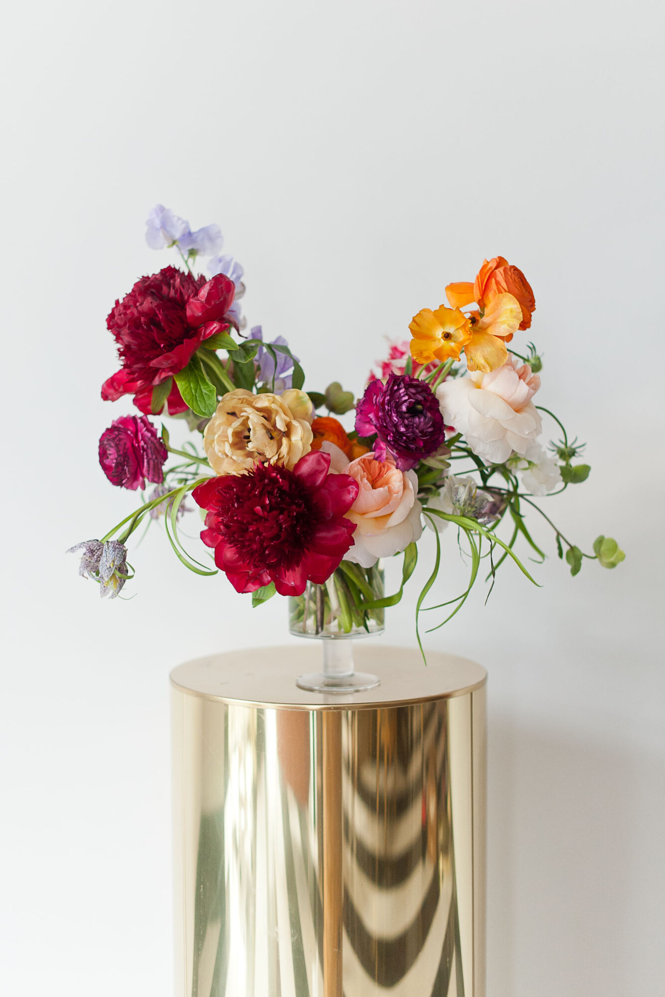 Colorful bouquet of flowers in a glass vase on a round table against a plain background.