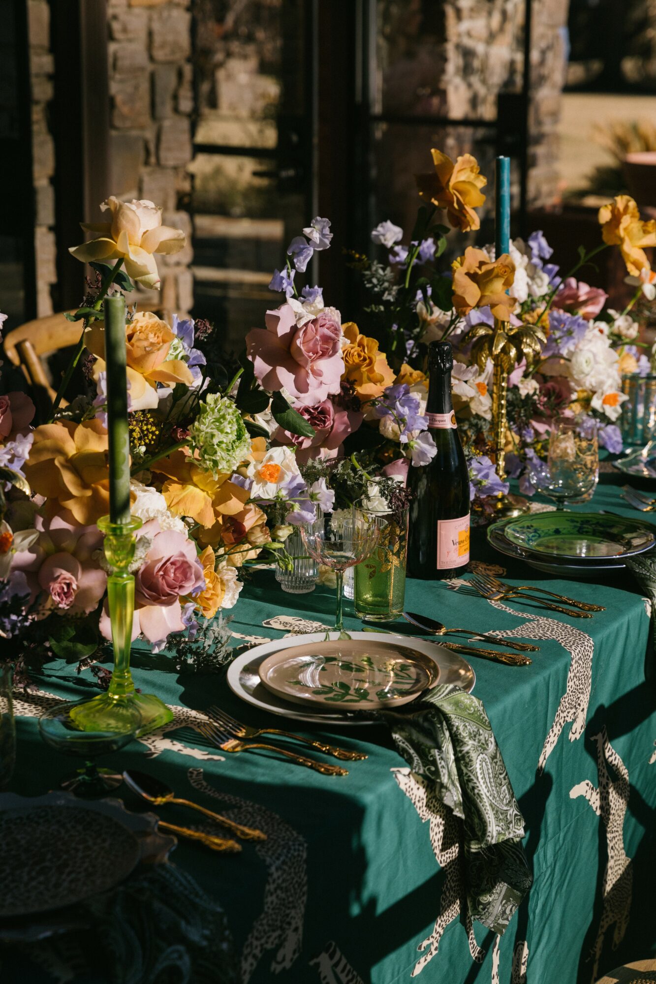 Table set with floral arrangements, plates, glasses, and cutlery outdoors, sunlight illuminating the scene.