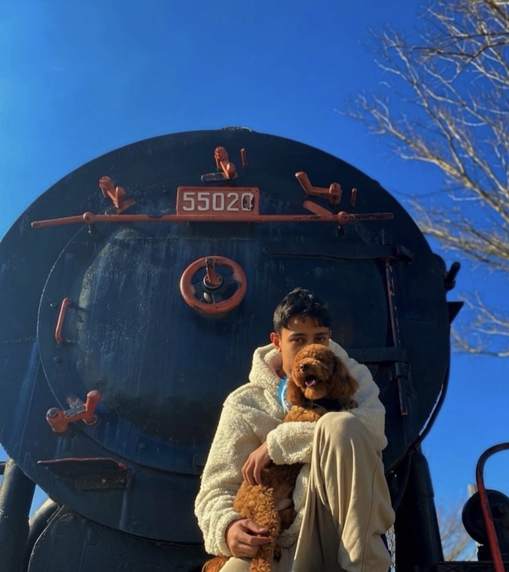 Person holding a dog in front of a large black steam locomotive with a blue sky background.
