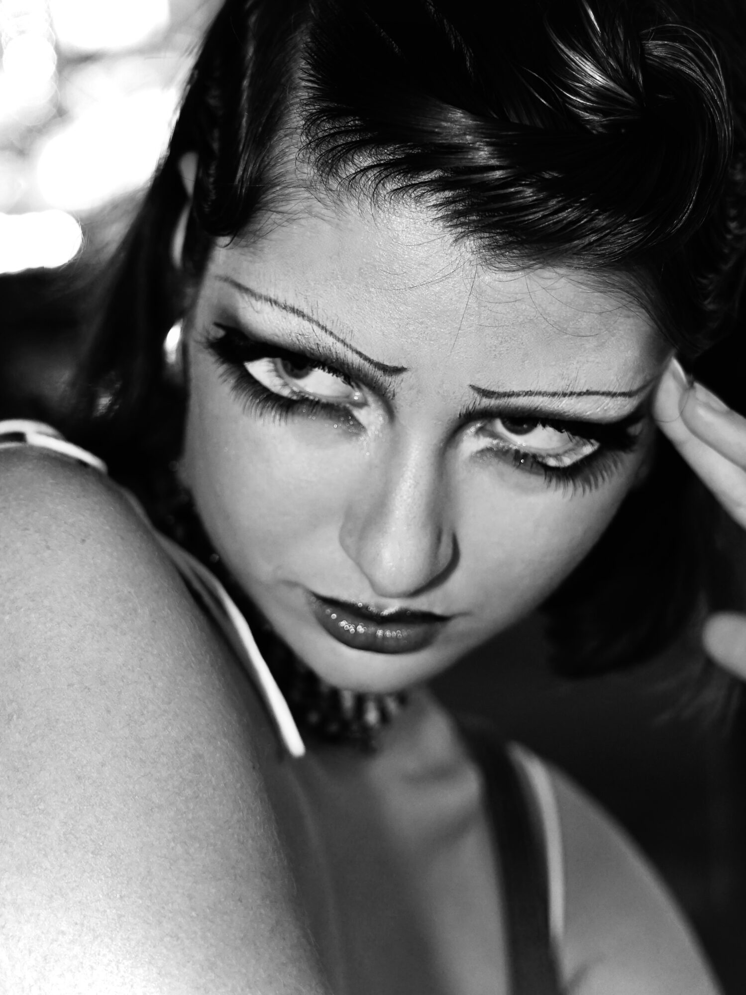 Close-up of a woman with dark hair, intense gaze, and makeup, looking slightly downward.