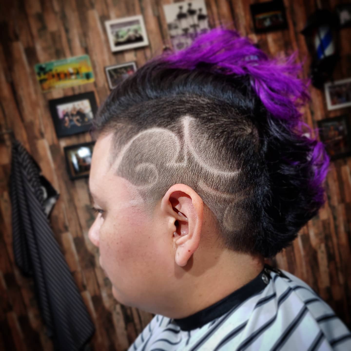 Side view of a person with a mohawk hairstyle featuring purple and black colors, with a shaved design on the side.
