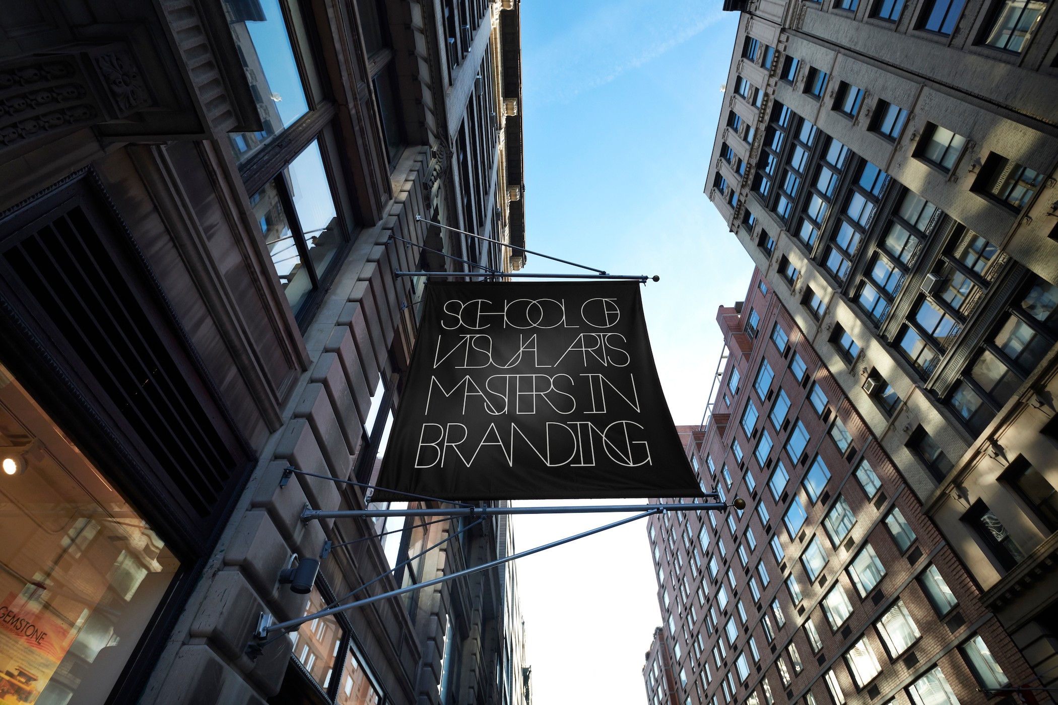 View looking up between tall buildings with a sign reading 'School of Arts Mastering Branding' in the sky.