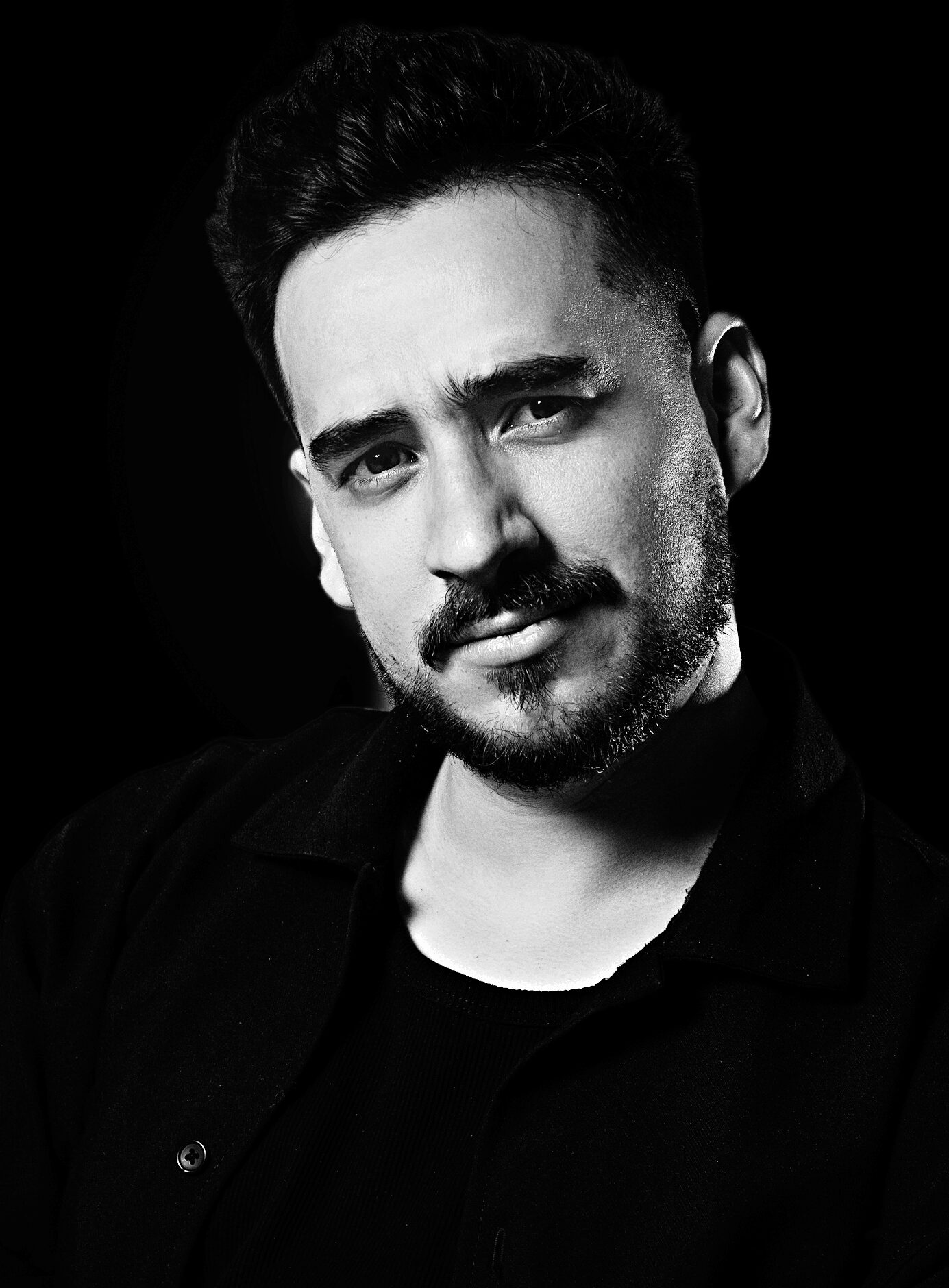 Black and white portrait of a man with dark hair and beard, looking at the camera with a serious expression.