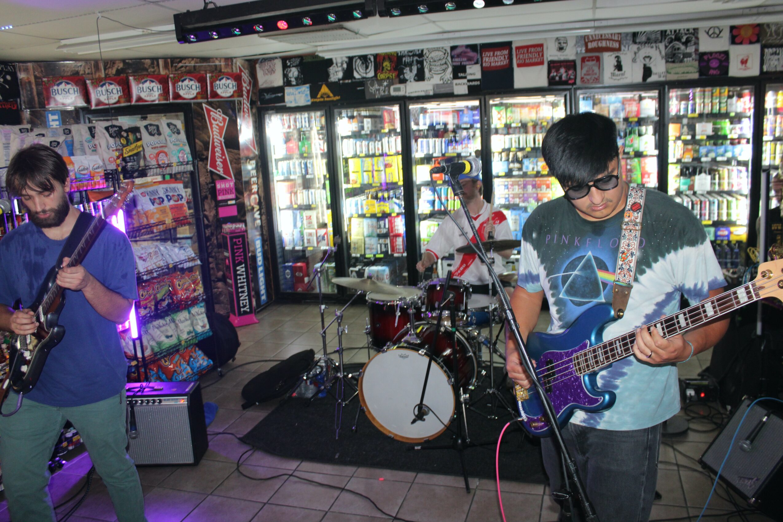 Three young men playing instruments in a store with shelves of products and vending machines in the background.