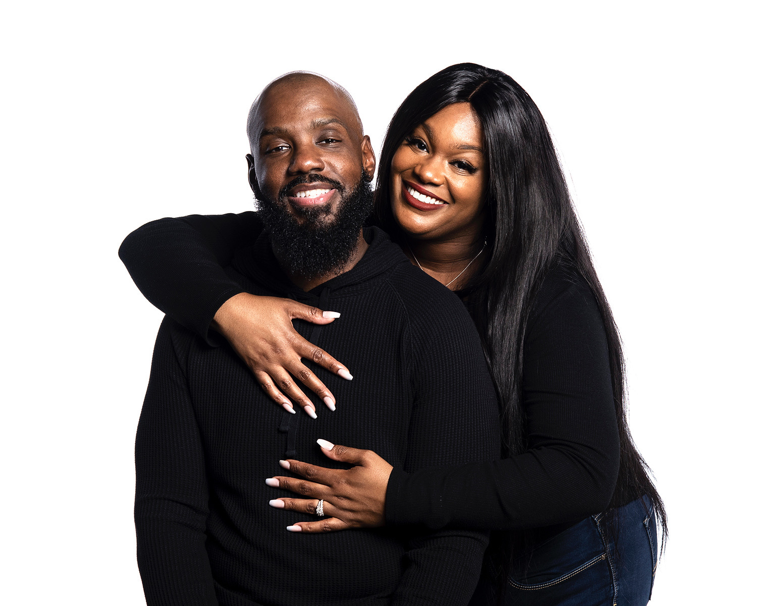A smiling couple with dark hair and skin, embracing each other against a white background.