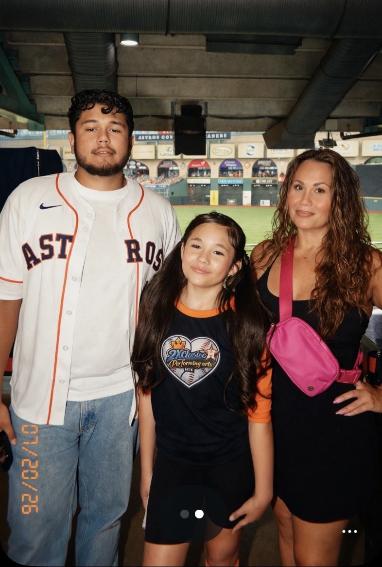 Three people, two adults and one child, standing outdoors with a stadium in the background.