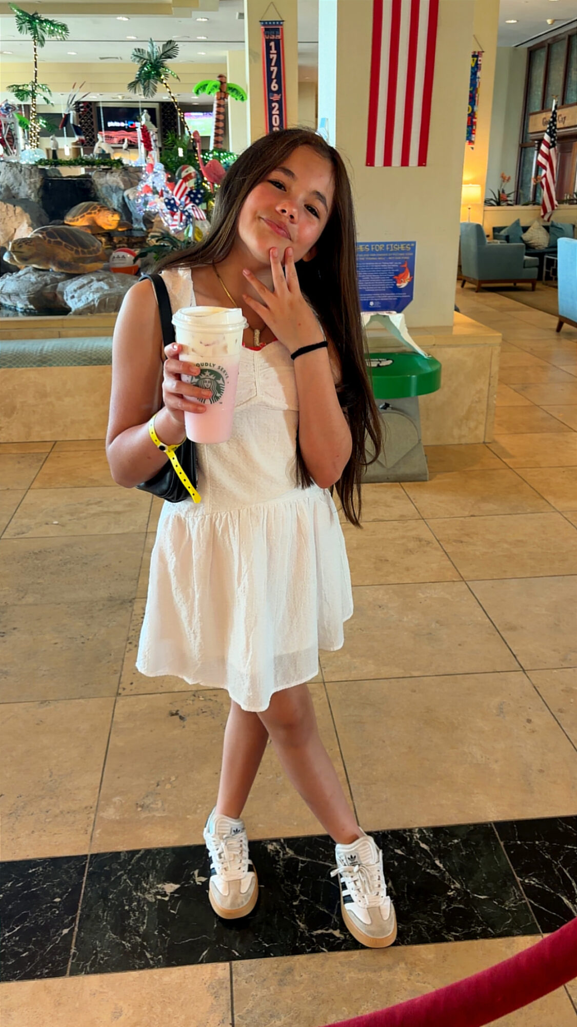 Young girl in white dress holding ice cream cone, smiling indoors with American flags and decorations in background.