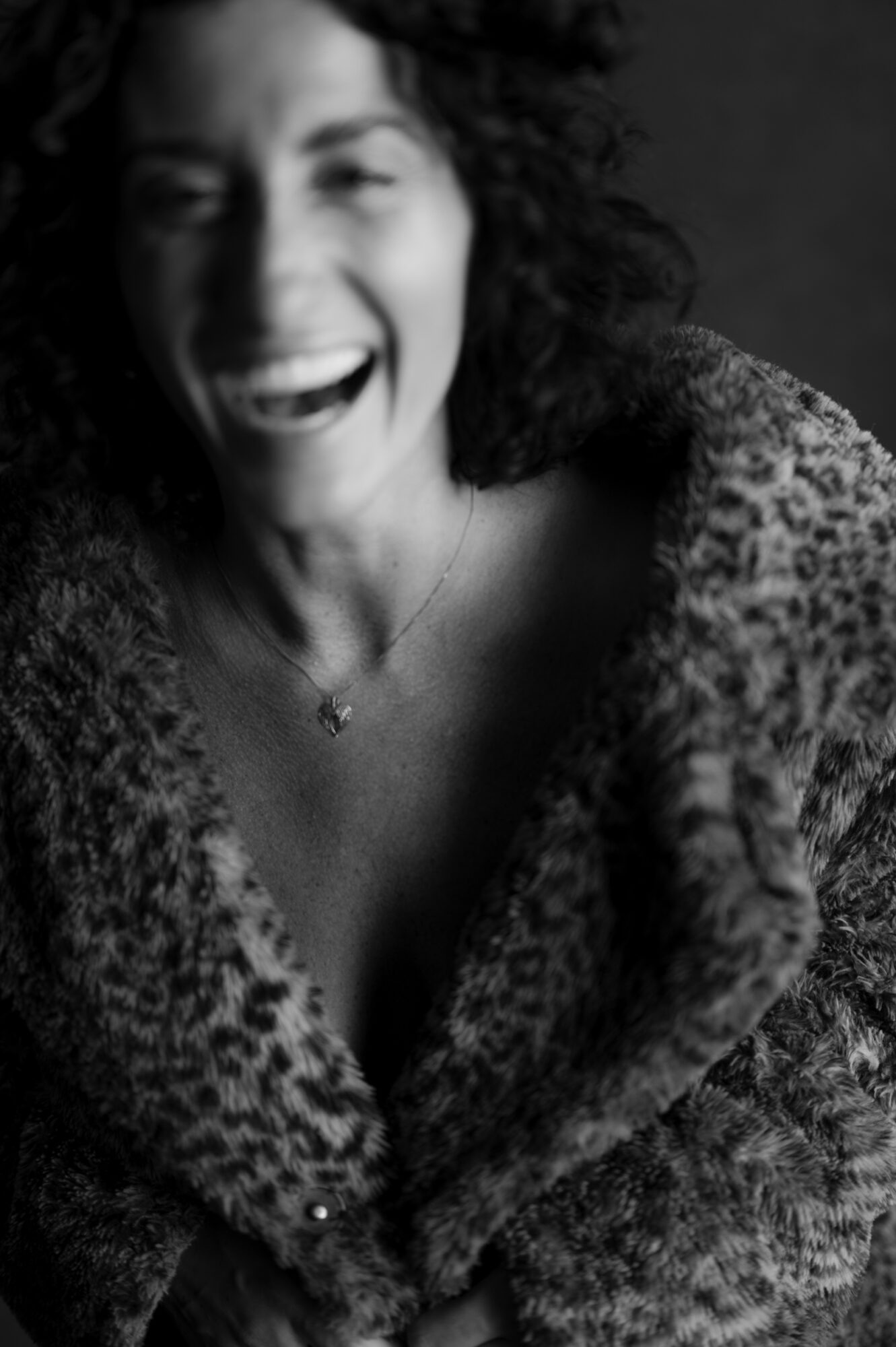 Woman with curly hair smiling, wearing a patterned top and a necklace, in black and white.