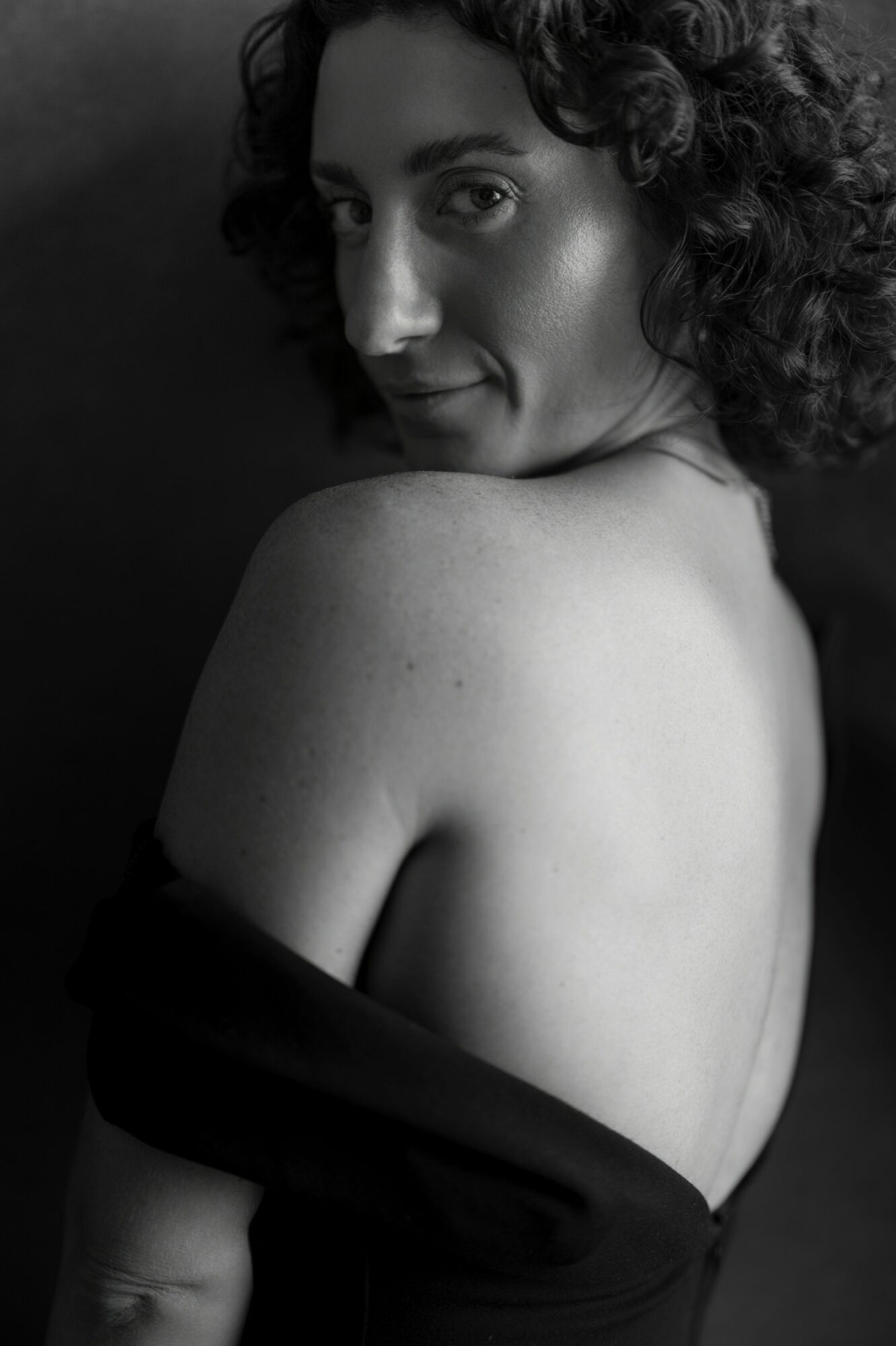 A woman with curly hair looks over her shoulder, partially covered by a black garment, in black and white.