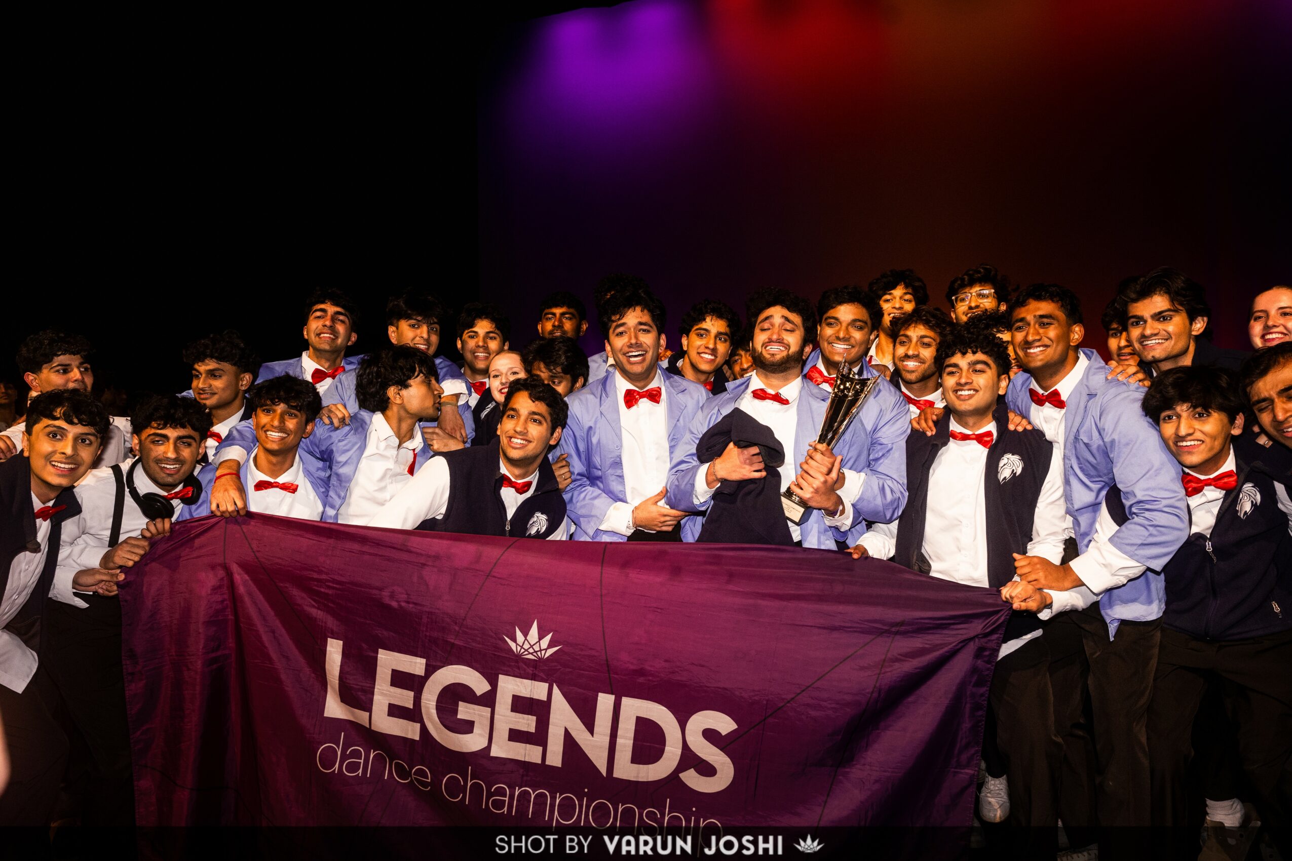 Group of young people holding a banner that reads 'LEGENDS dance championship' on stage, smiling and celebrating.