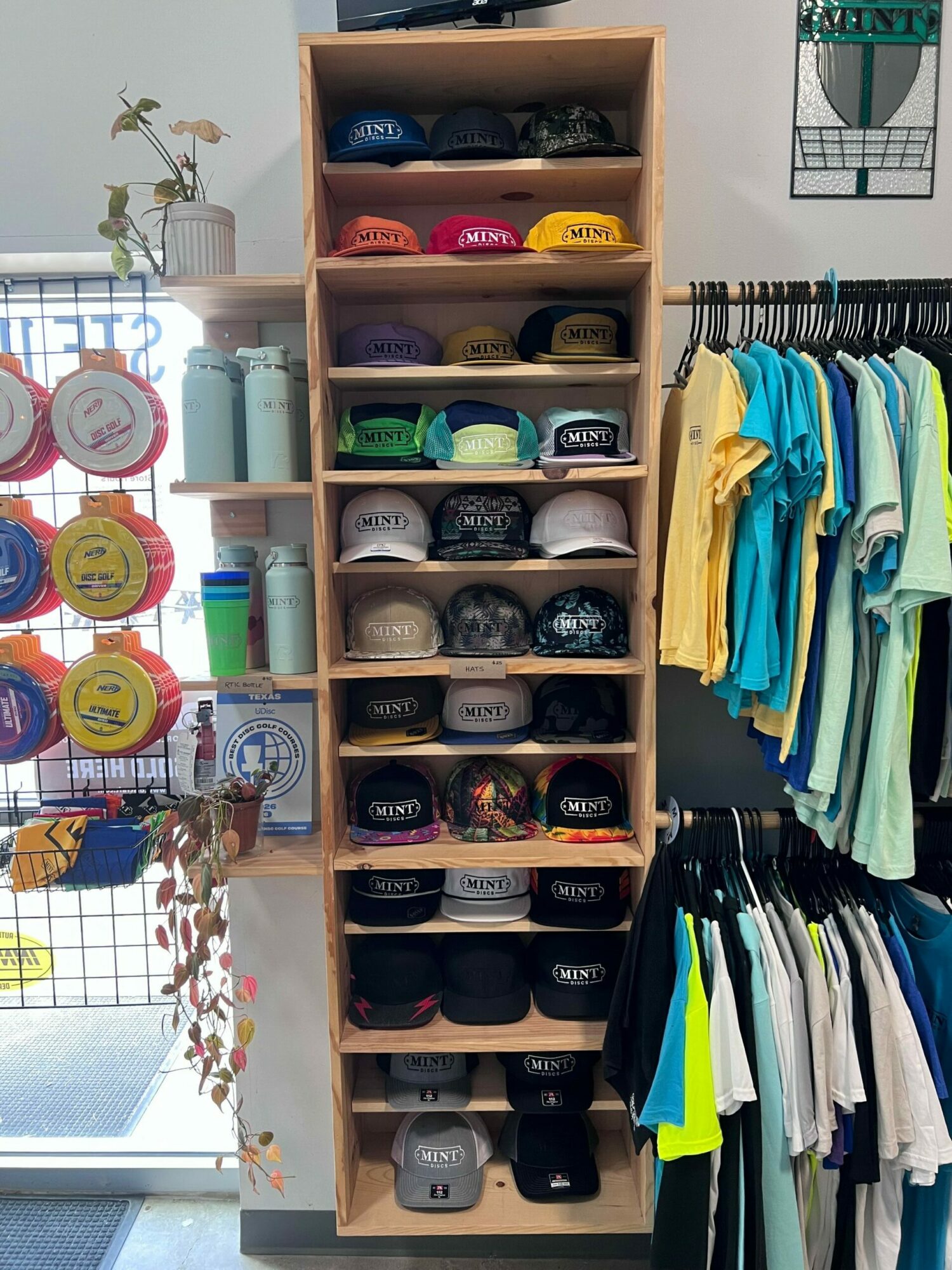 Shelves with neatly stacked fabric and paper supplies, with decorative plants and colorful objects in the background.
