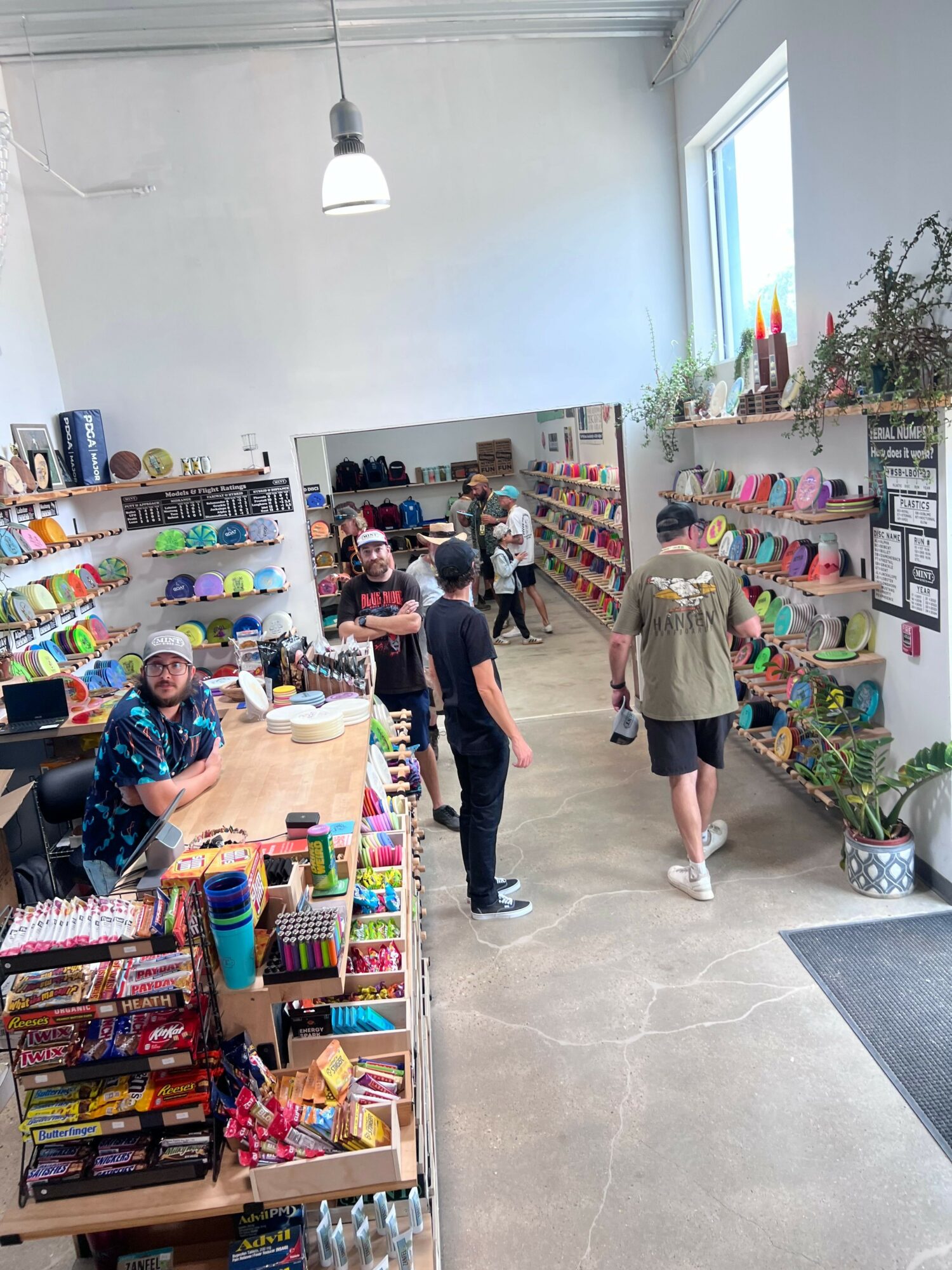 People shopping in a store with shelves of colorful products, some browsing and others checking items out, in a well-lit space.