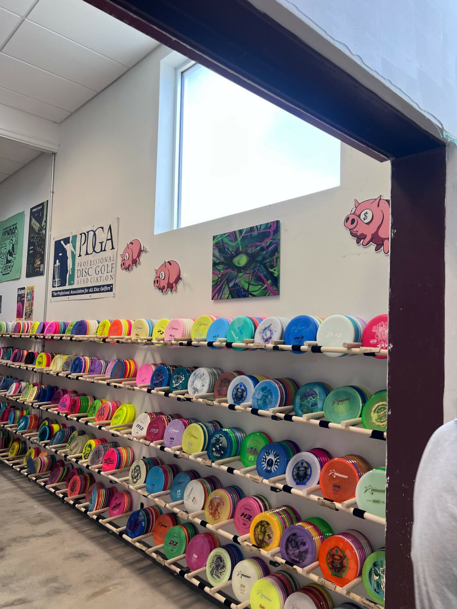 Colorful spools of thread arranged on shelves in a craft room, with a window and artwork on the wall.