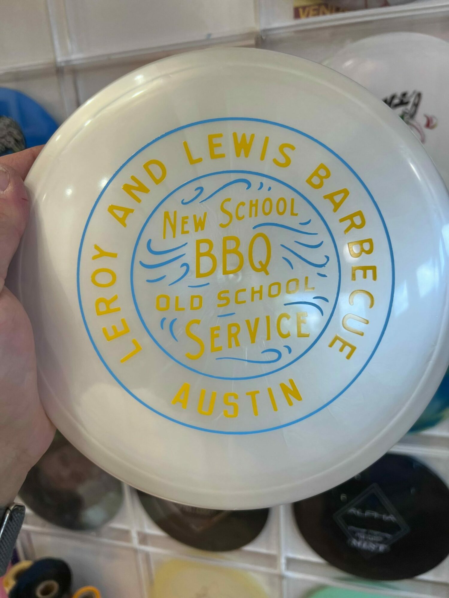 Round white plate with blue and yellow text and logo, held by a hand, with a storage area in the background.