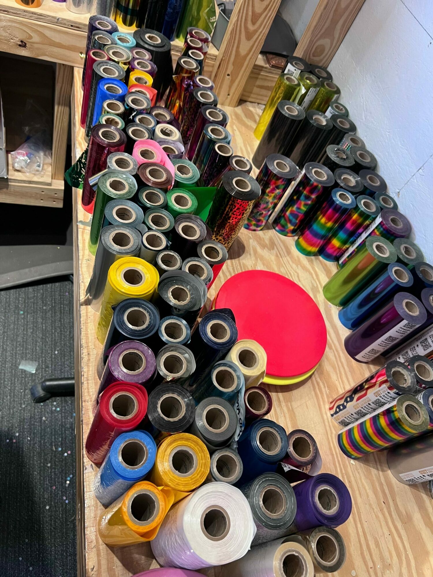 Wooden table with colorful rolls of tape and a red circular object, against a wall with a picture frame.